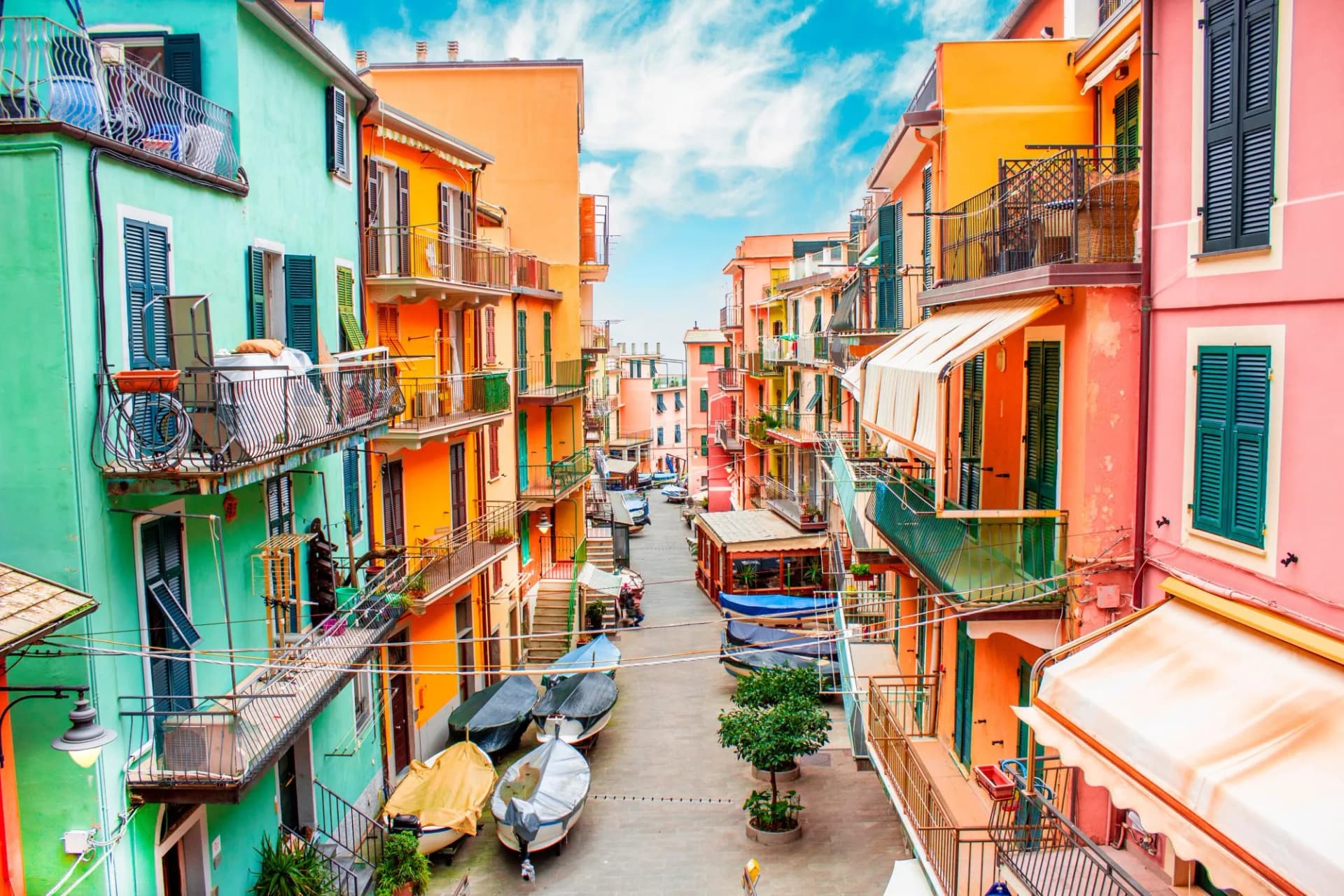 Colorful buildings line a narrow street in Manarola, Cinque Terre, with fishing boats parked on the pavement.