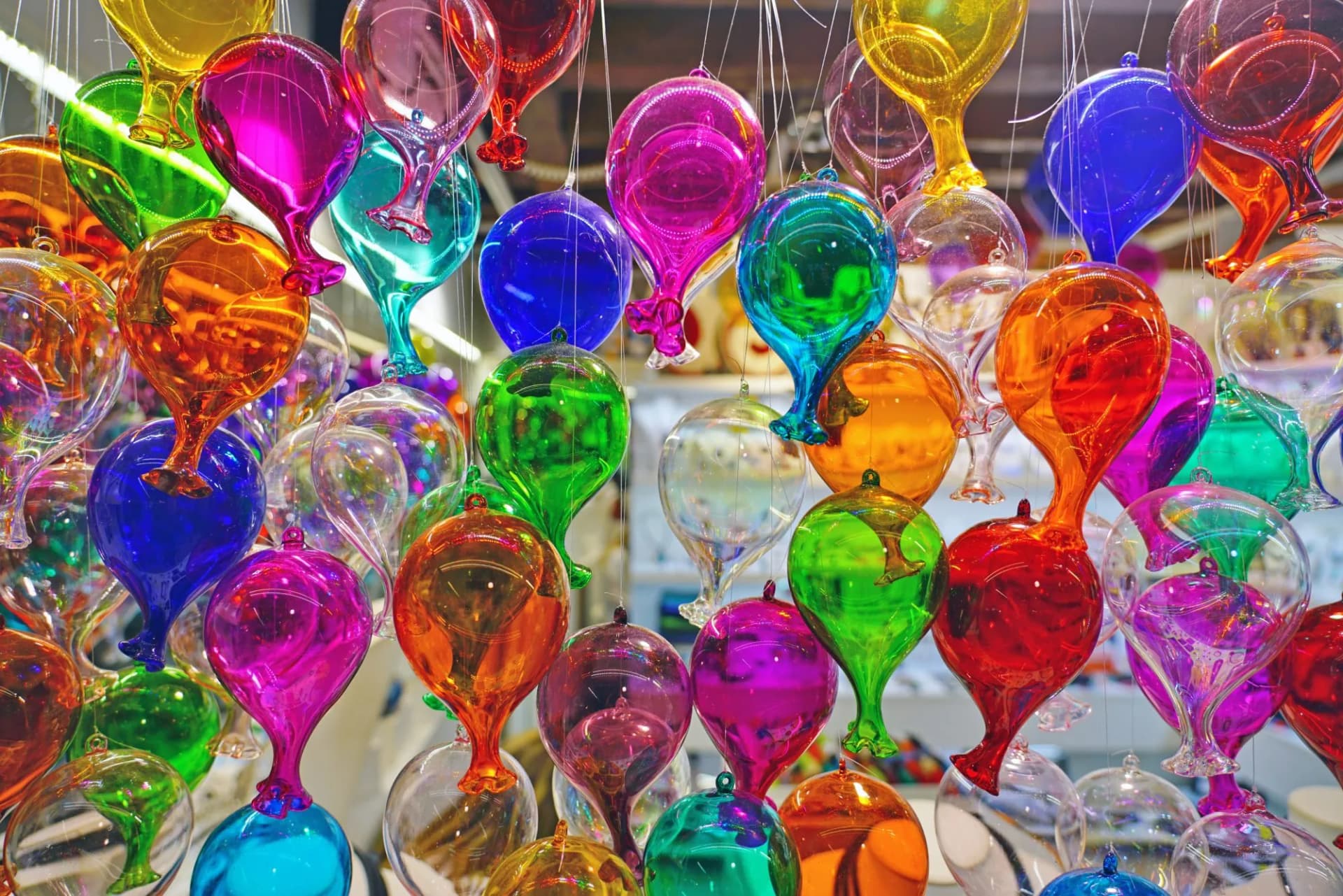 Hanging display of colorful, reflective Murano glass decorative balloons in various shapes.