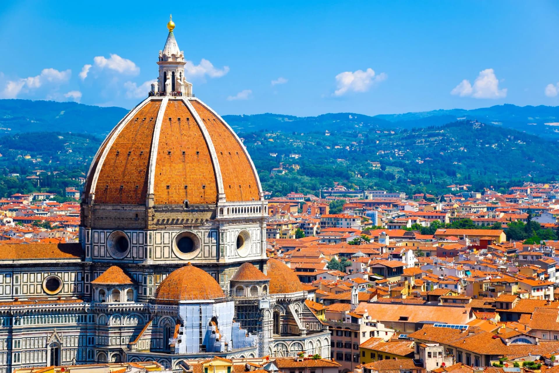 Close-up of the Cathedral of Santa Maria del Fiore dome over Florence old town and green hills.