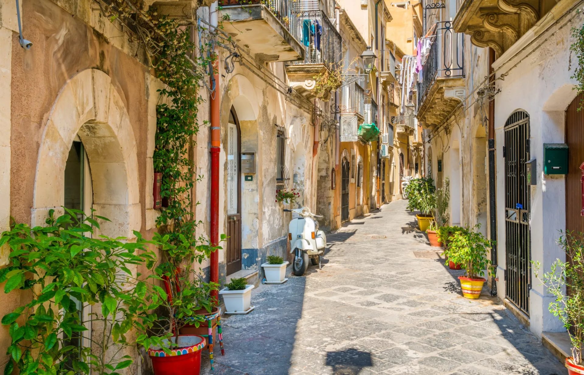 Narrow street in Ortigia, Siracusa old town with potted plants and a parked white scooter.