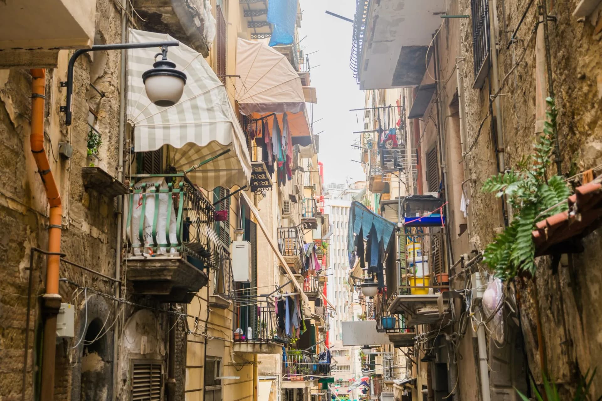 Narrow, crowded city street in Naples, Italy, lined with old buildings, balconies, and hanging laundry.