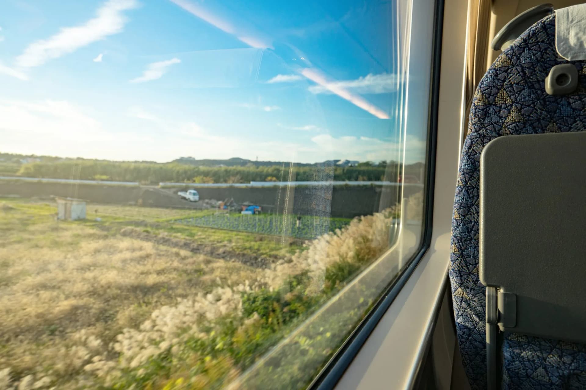 View from train window overlooking dry grass, small farm, and blue sky.