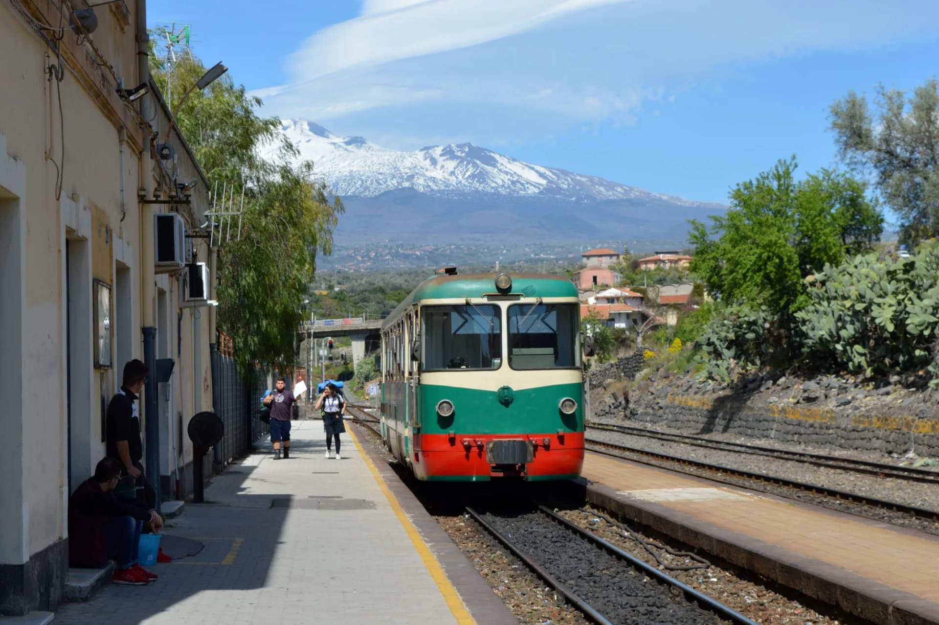 Old green and red train at Paterno station with Mount Etna snow-capped in the background, Sicily.