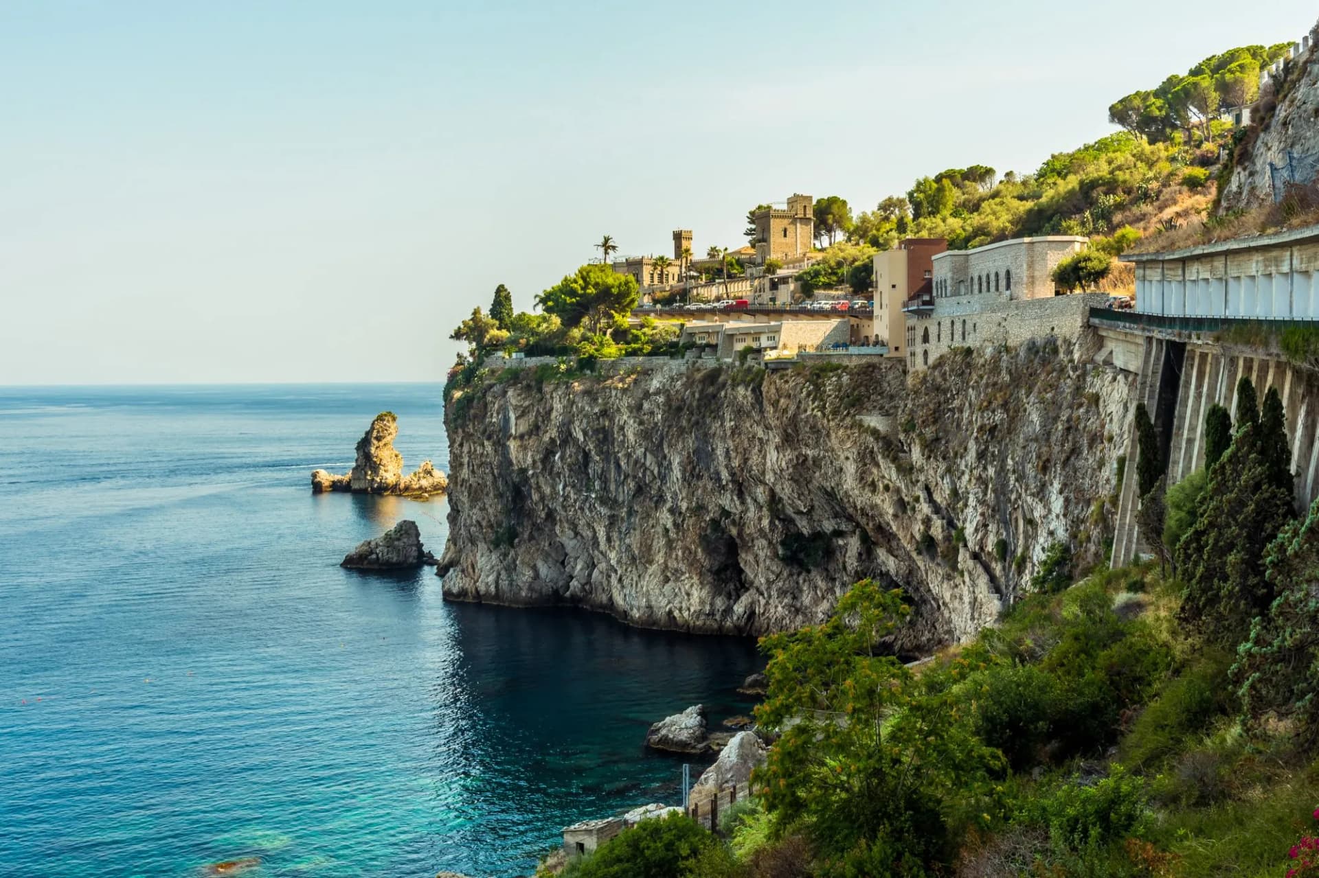 Cliffs along the shoreline at Taormina, Sicily with buildings atop and sea stacks in summer.