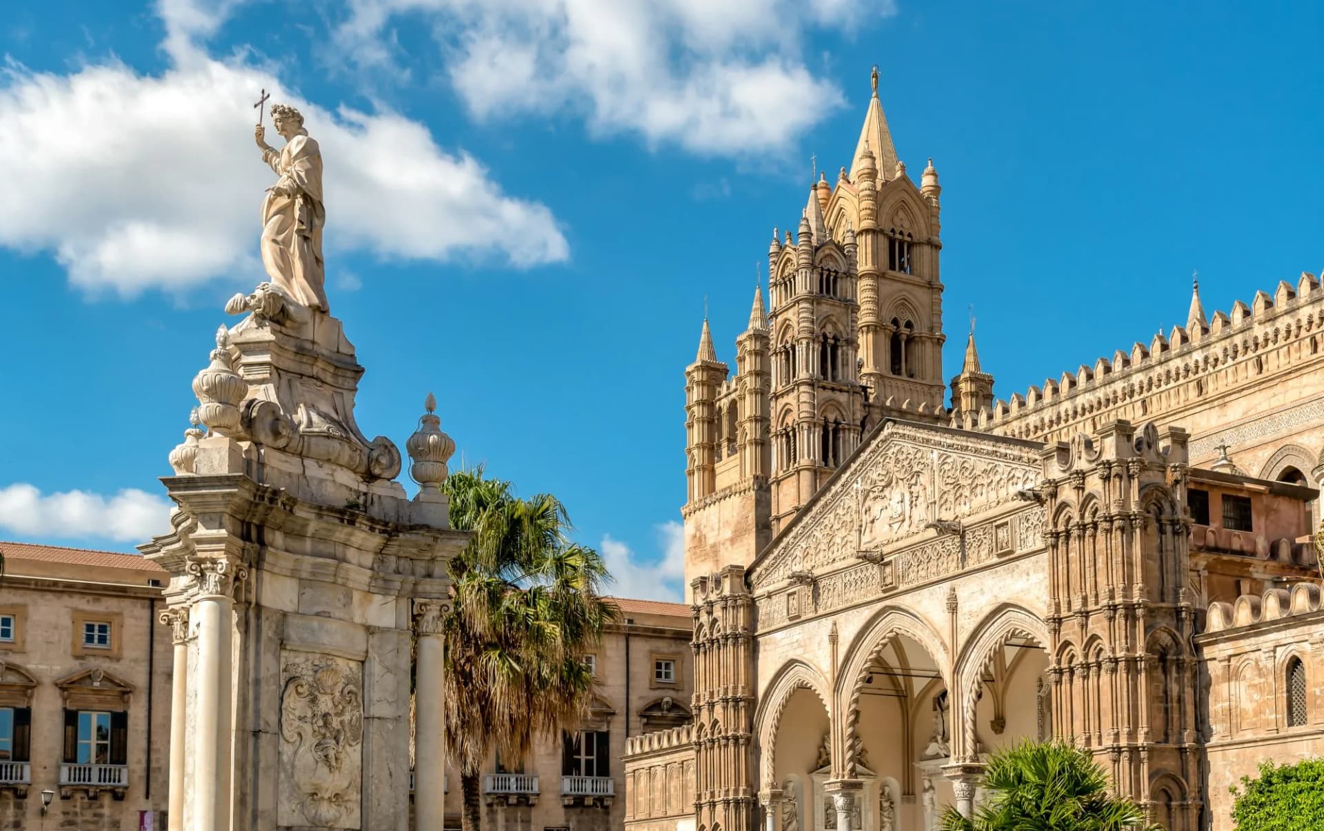 Palermo Cathedral with Santa Rosalia statue and palm trees under blue sky, Sicily.