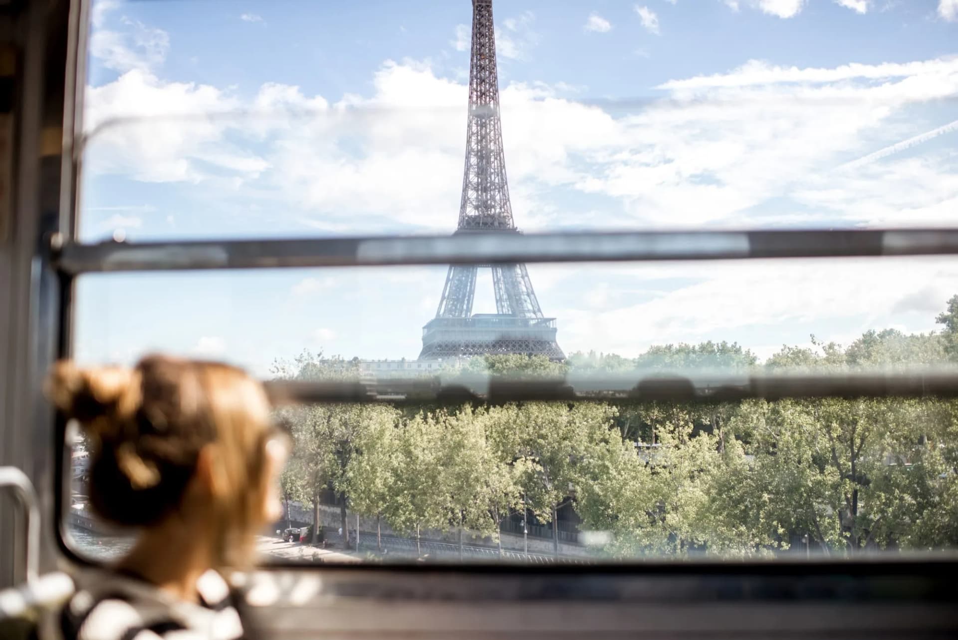 Young woman viewing the Eiffel Tower through a train window in Paris over green trees.