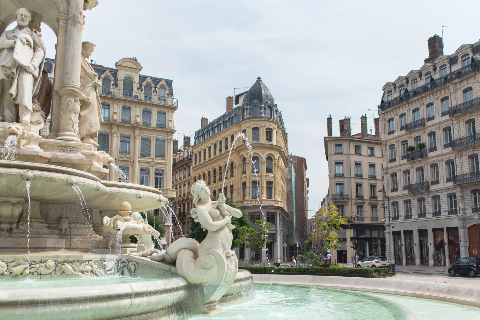 Fountain with statues and water jets in Place des Jacobins, Lyon, surrounded by historic facades.