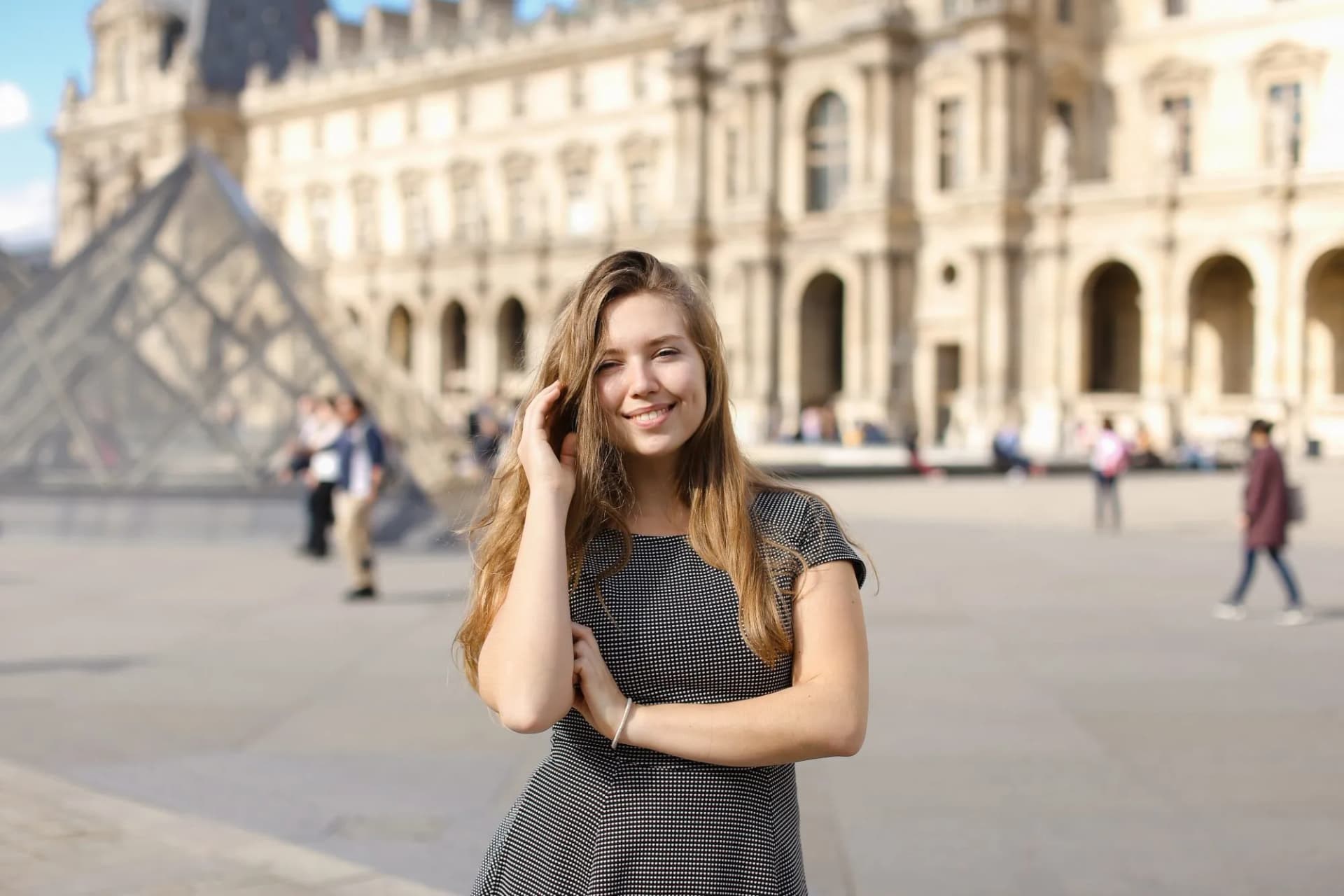 Smiling woman near Louvre Pyramid with historic building in Paris background