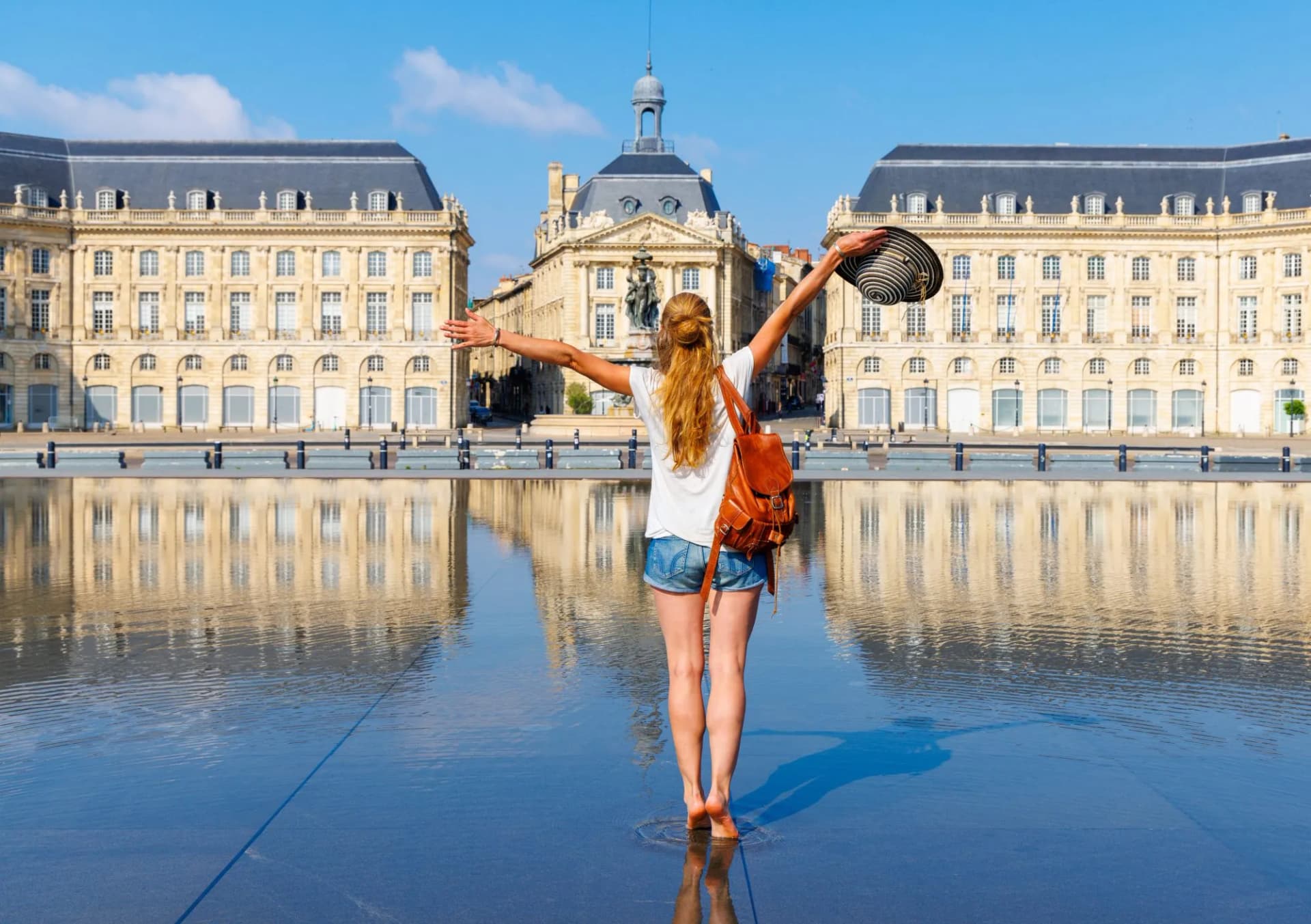 Traveler with arms outstretched at Bordeaux Bourse Square water mirror, France