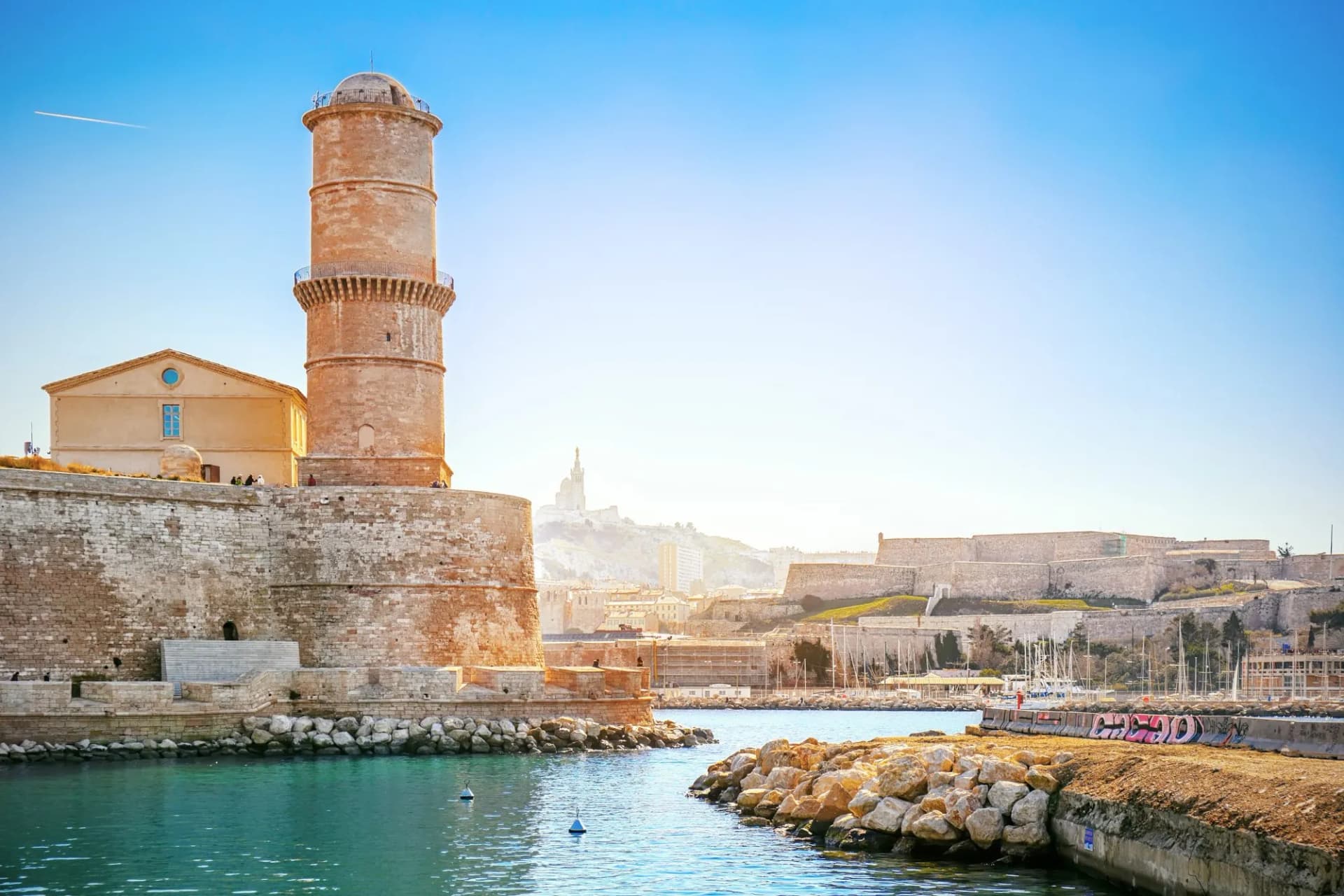 Fort Saint-Jean tower in Marseille harbor with Notre-Dame de la Garde visible on the hill.