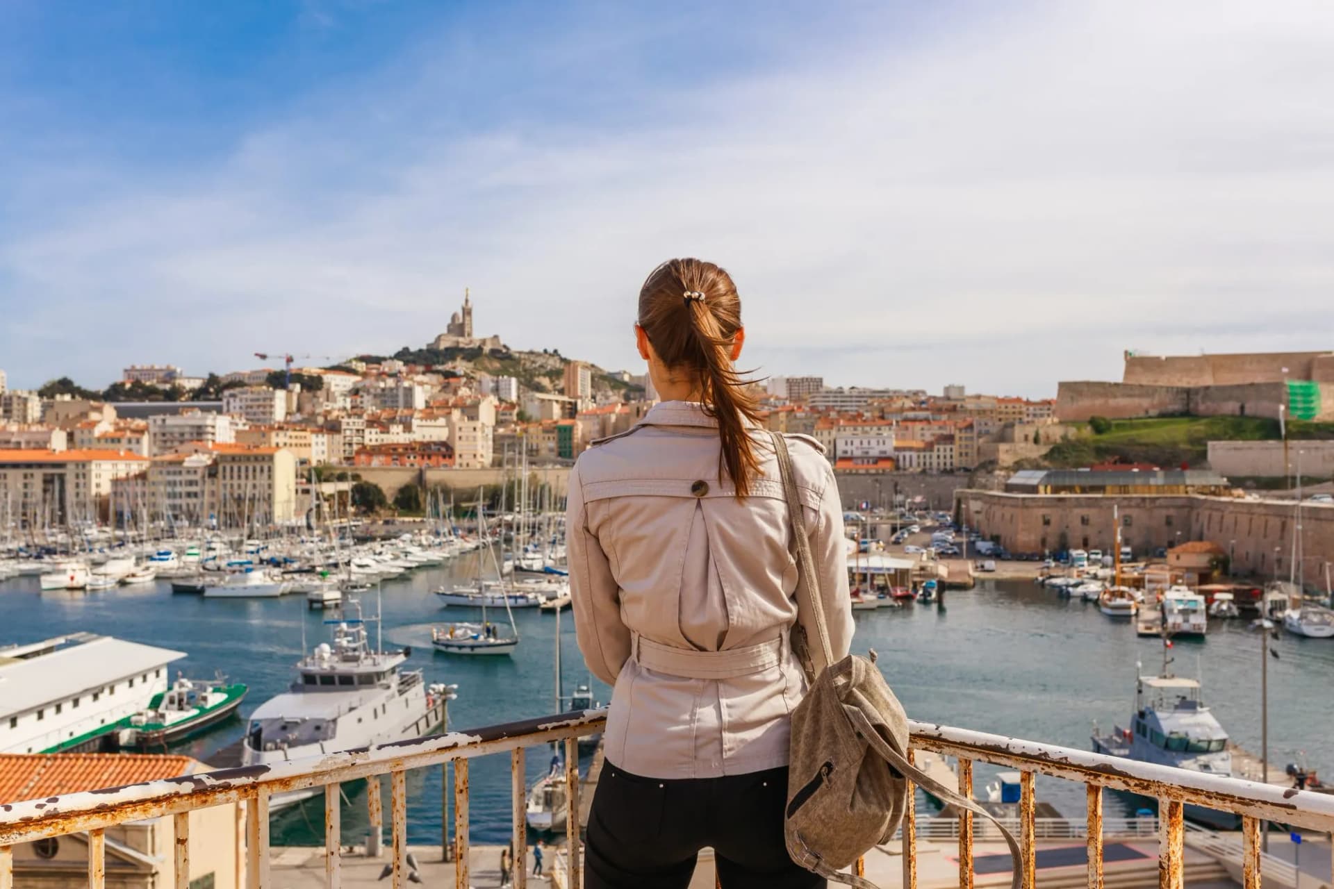 Tourist viewing Marseille harbor with boats, city skyline, and Notre-Dame de la Garde.