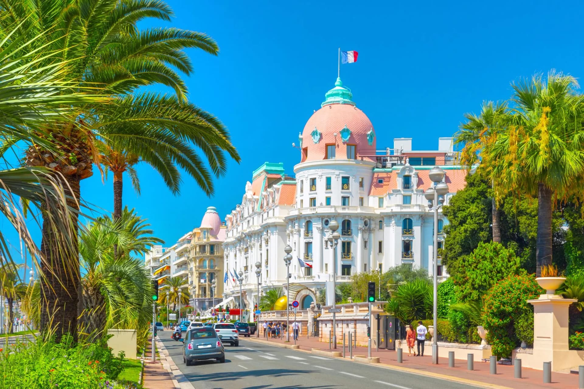 Promenade des Anglais in Nice, France, with palm trees and a grand white hotel.