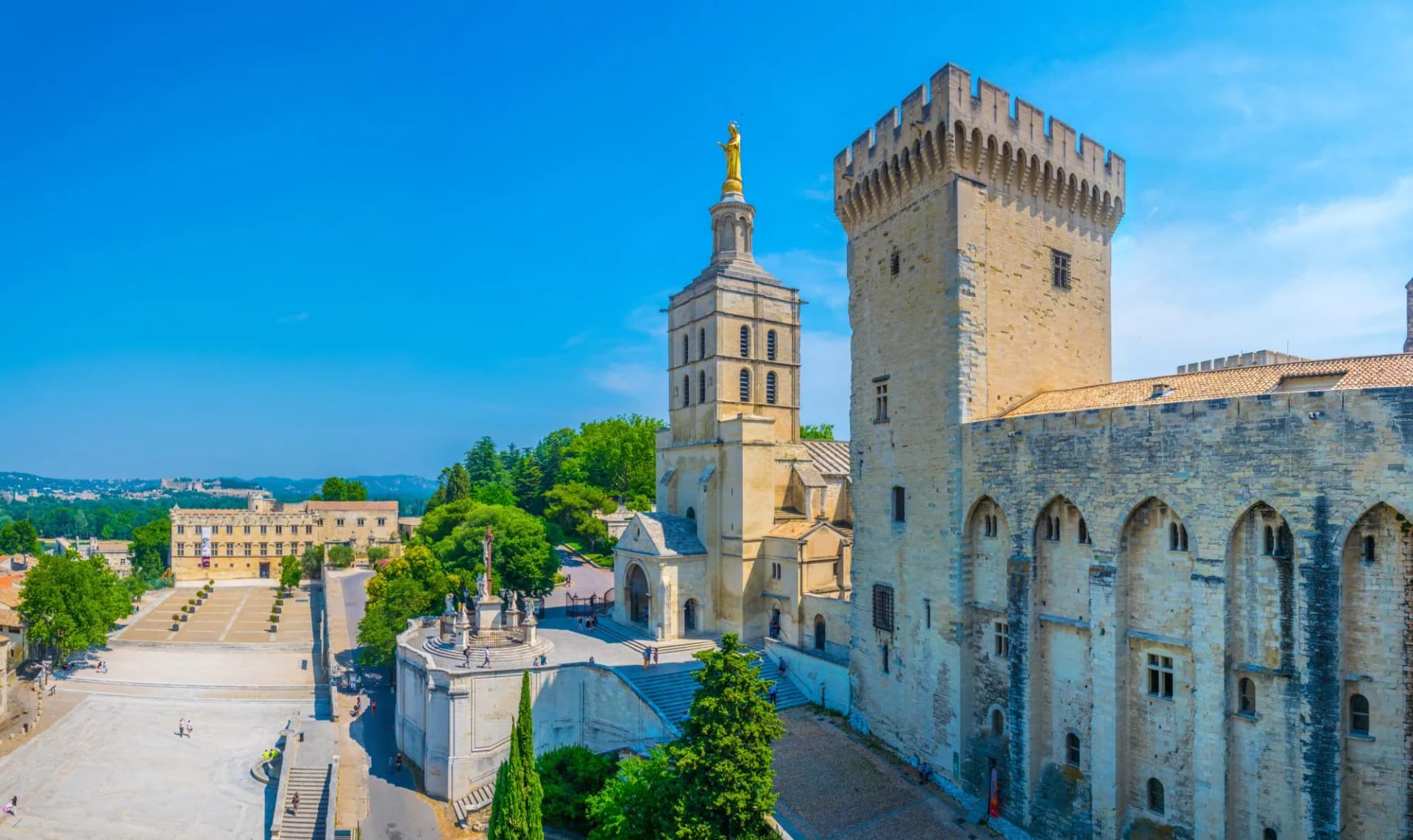 Palais des Papes and Avignon Cathedral with golden statue under a clear blue sky in France.