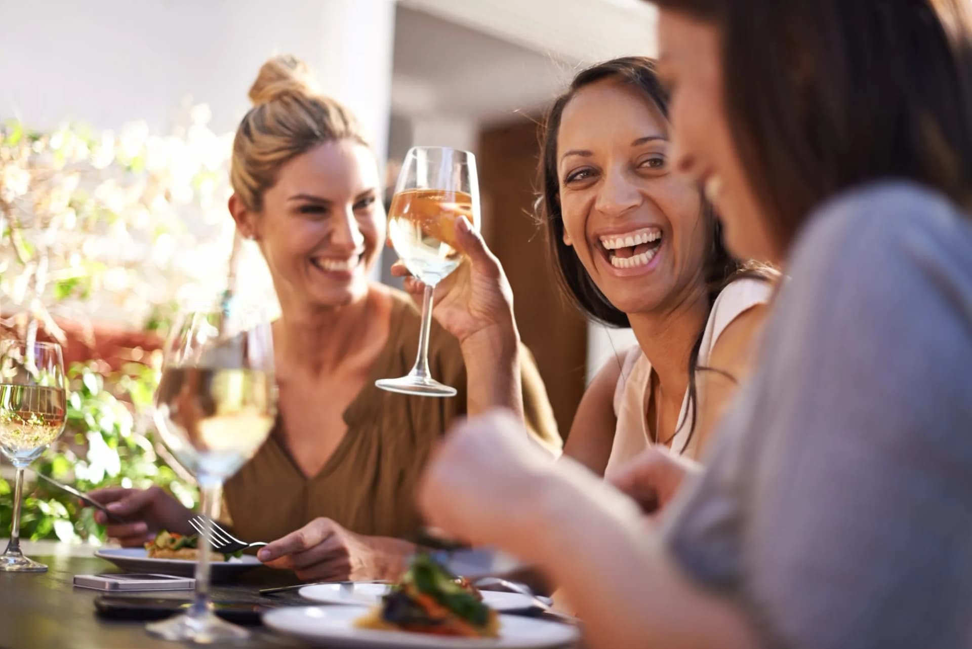 Friends laughing and drinking white wine together during an outdoor meal.