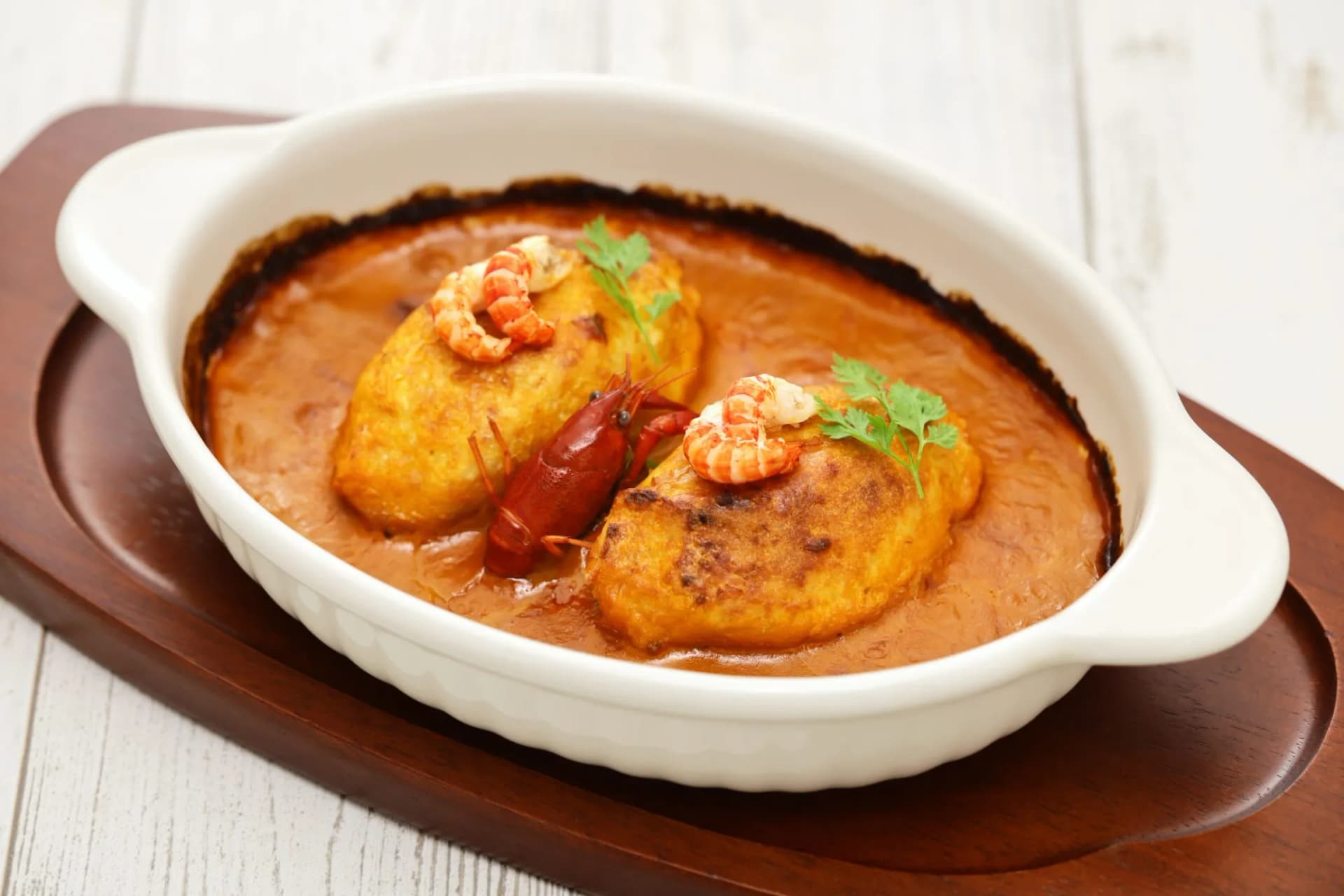 Homemade quenelle dumplings with crayfish in creamy sauce, served in a white dish on wood.