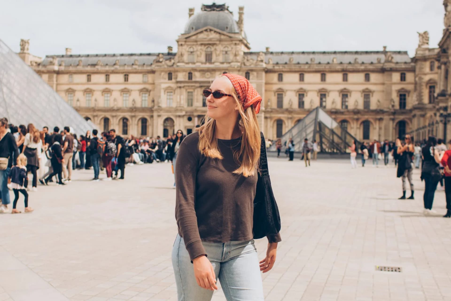 Woman tourist with red kerchief at the Louvre Museum in Paris with crowds.
