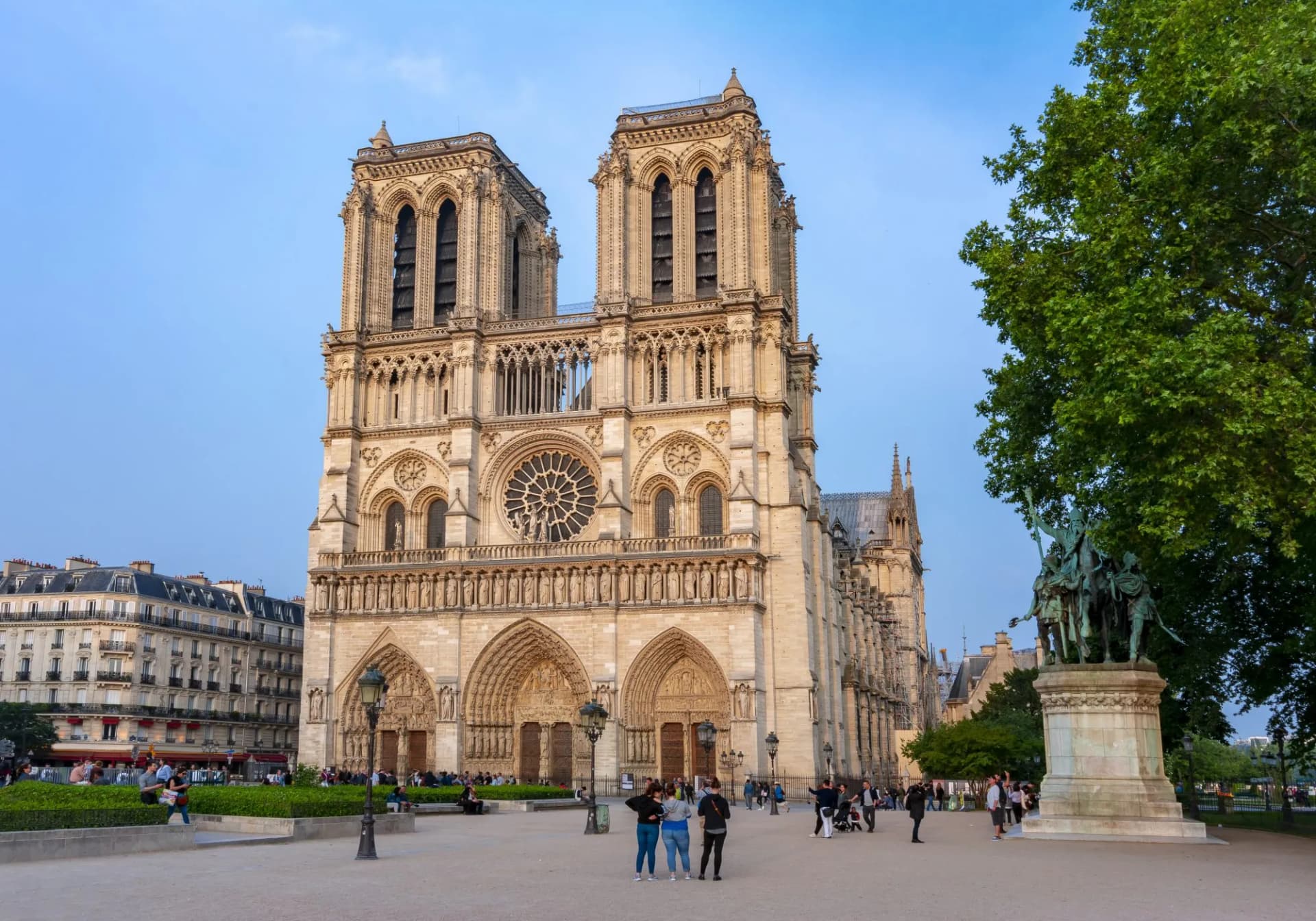 Notre Dame de Paris Cathedral facade with people in square and equestrian statue in Paris.