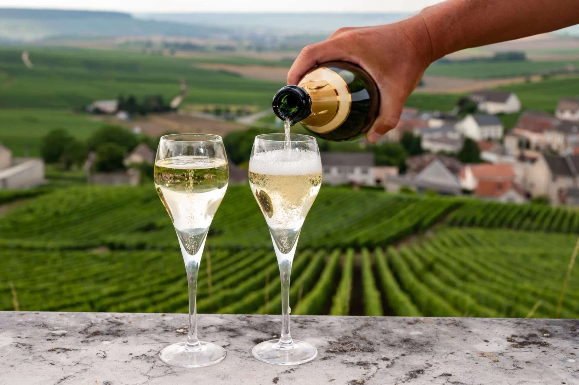 Pouring sparkling wine into flute glasses overlooking Cramant, France vineyards.