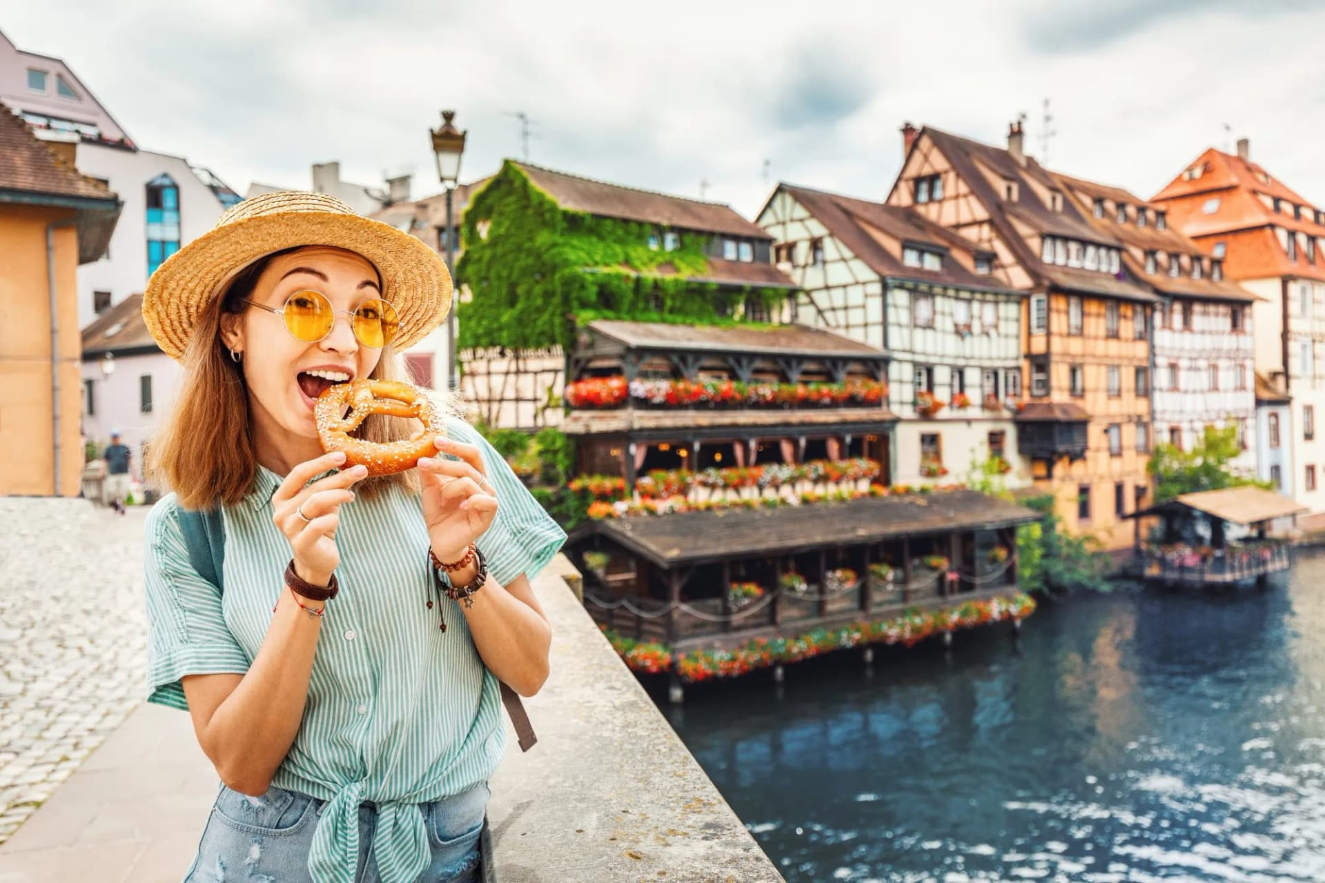 Tourist eating pretzel on bridge near half-timbered buildings over canal in Europe