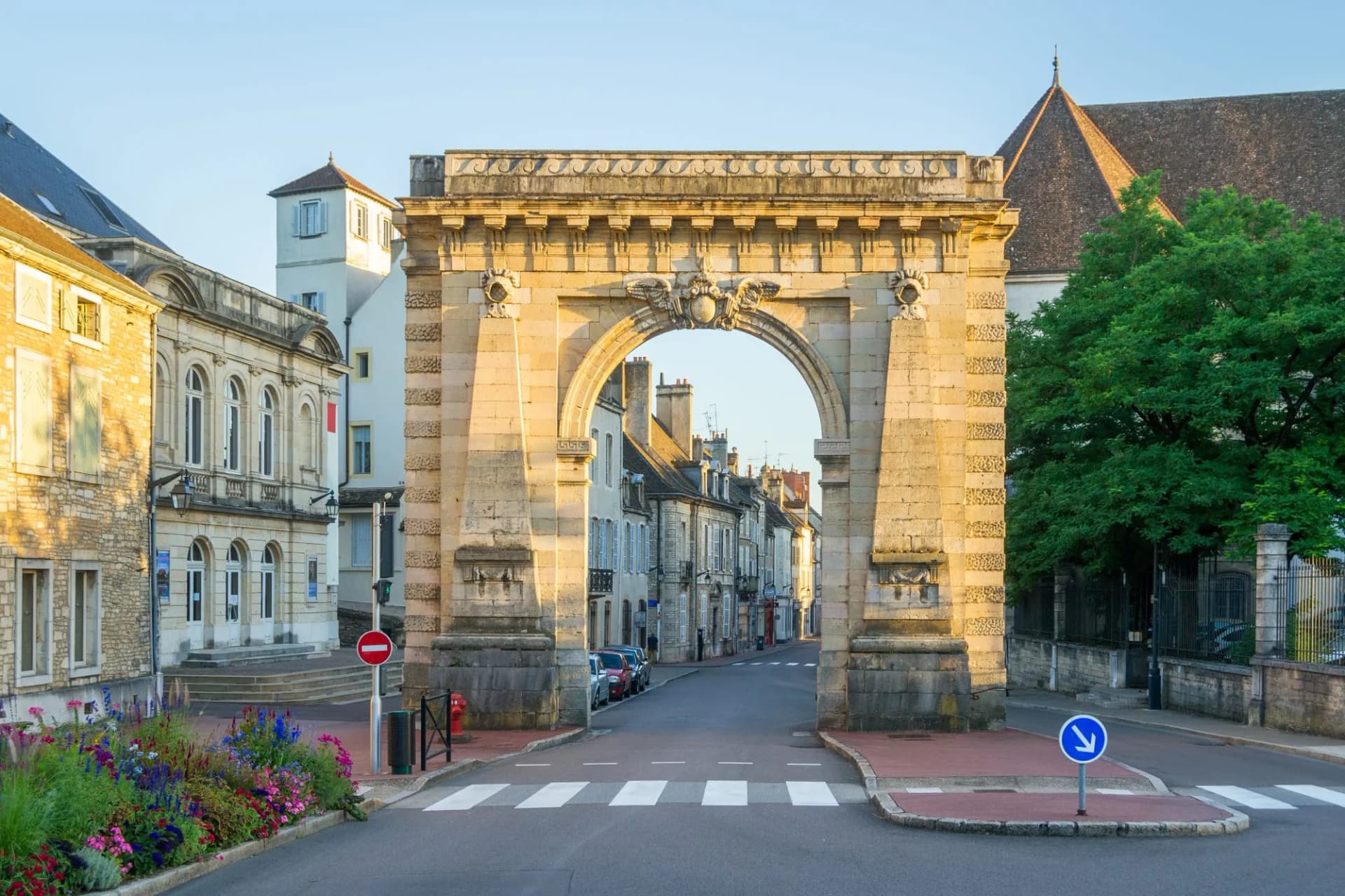 Stone archway entrance to Beaune street with historic buildings and summer flowers.