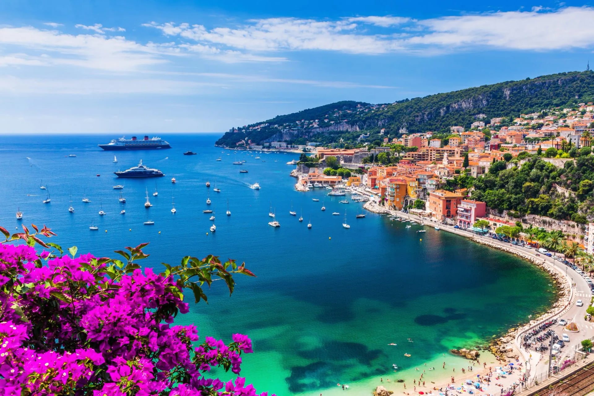 Villefranche-sur-Mer seaside town on the French Riviera with colorful buildings, boats, and purple flowers.