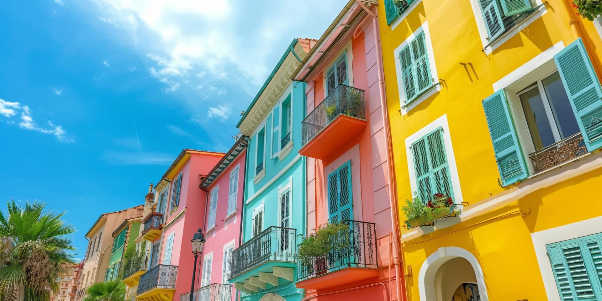 Vibrant historic homes with colorful facades and teal shutters in Nice's Old Town under a bright blue sky.