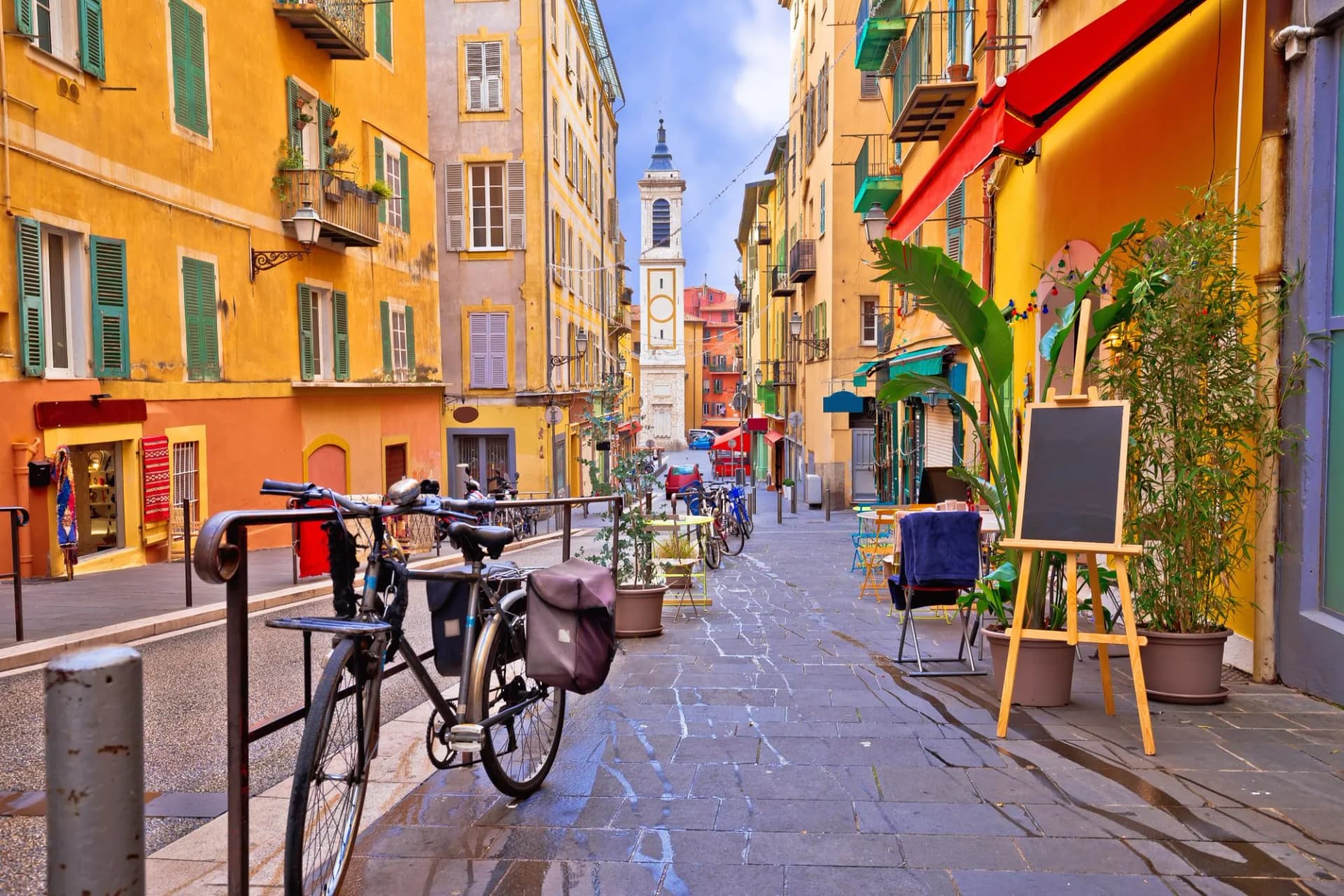 Colorful street architecture leads to a church tower in a European old town with a bicycle parked.