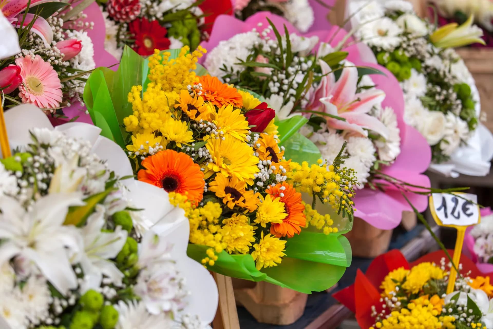 Various colorful flower bouquets, including yellow and orange gerberas, displayed at the Cours Saleya market in Nice, France.