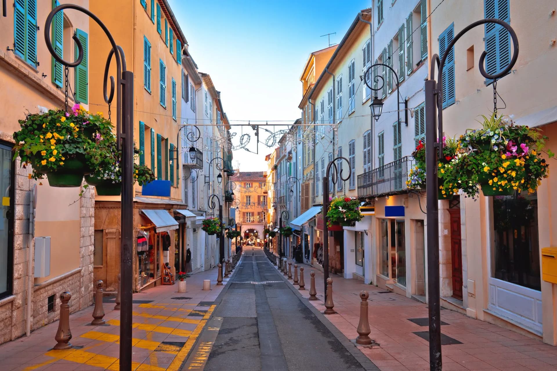 Colorful street in Antibes with shops, flower baskets, and wrought iron lampposts.