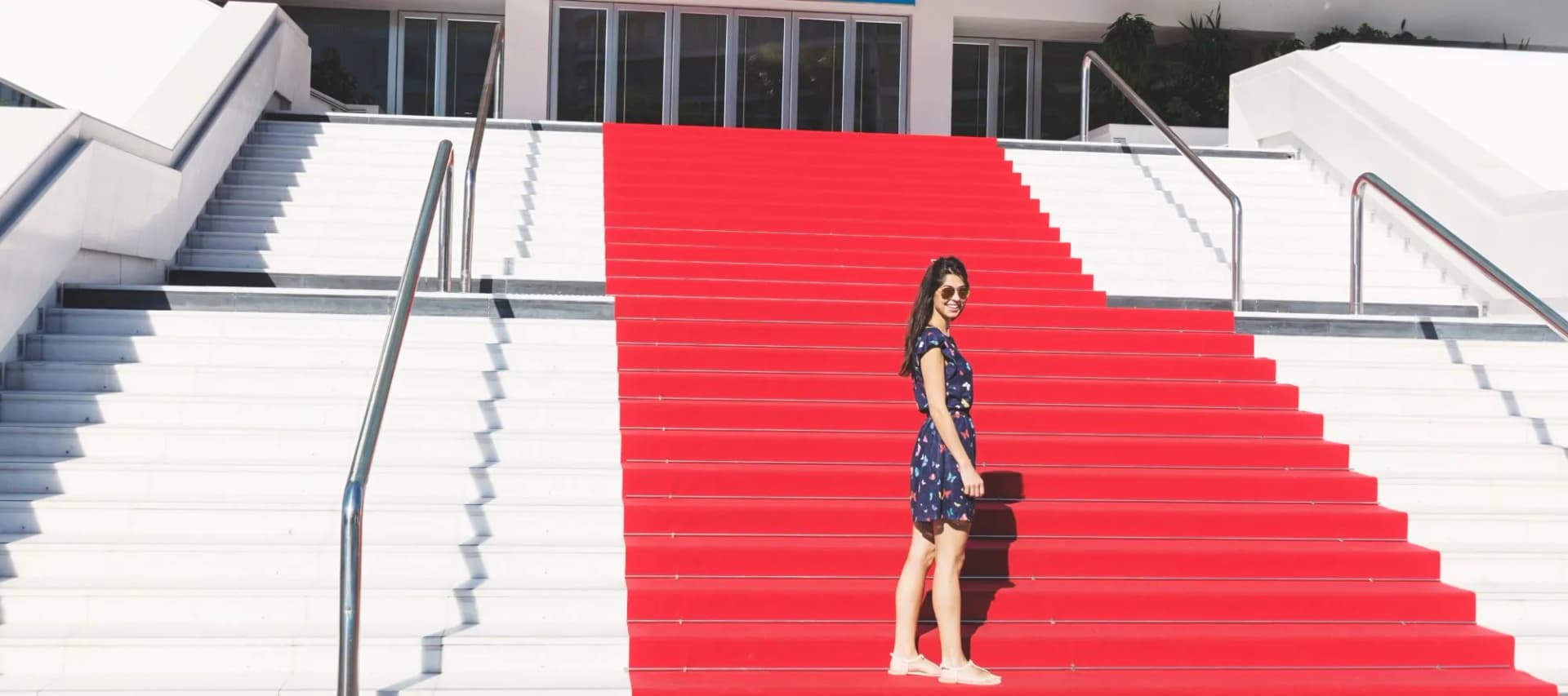 Woman posing on grand staircase with half white marble and half red carpet steps in Cannes, France.