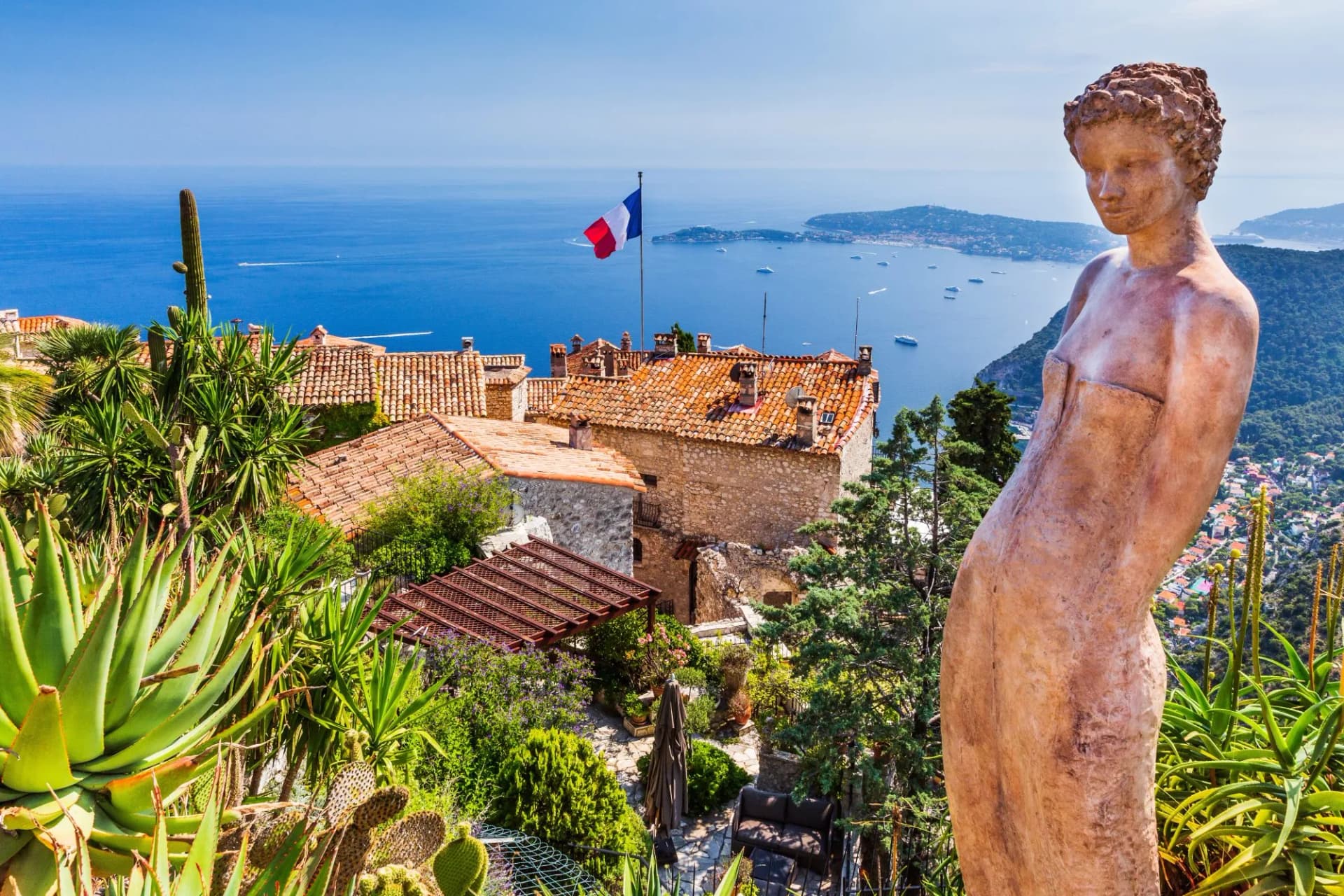 Statue overlooking Eze medieval town, French Riviera, with terracotta roofs and blue Mediterranean Sea.