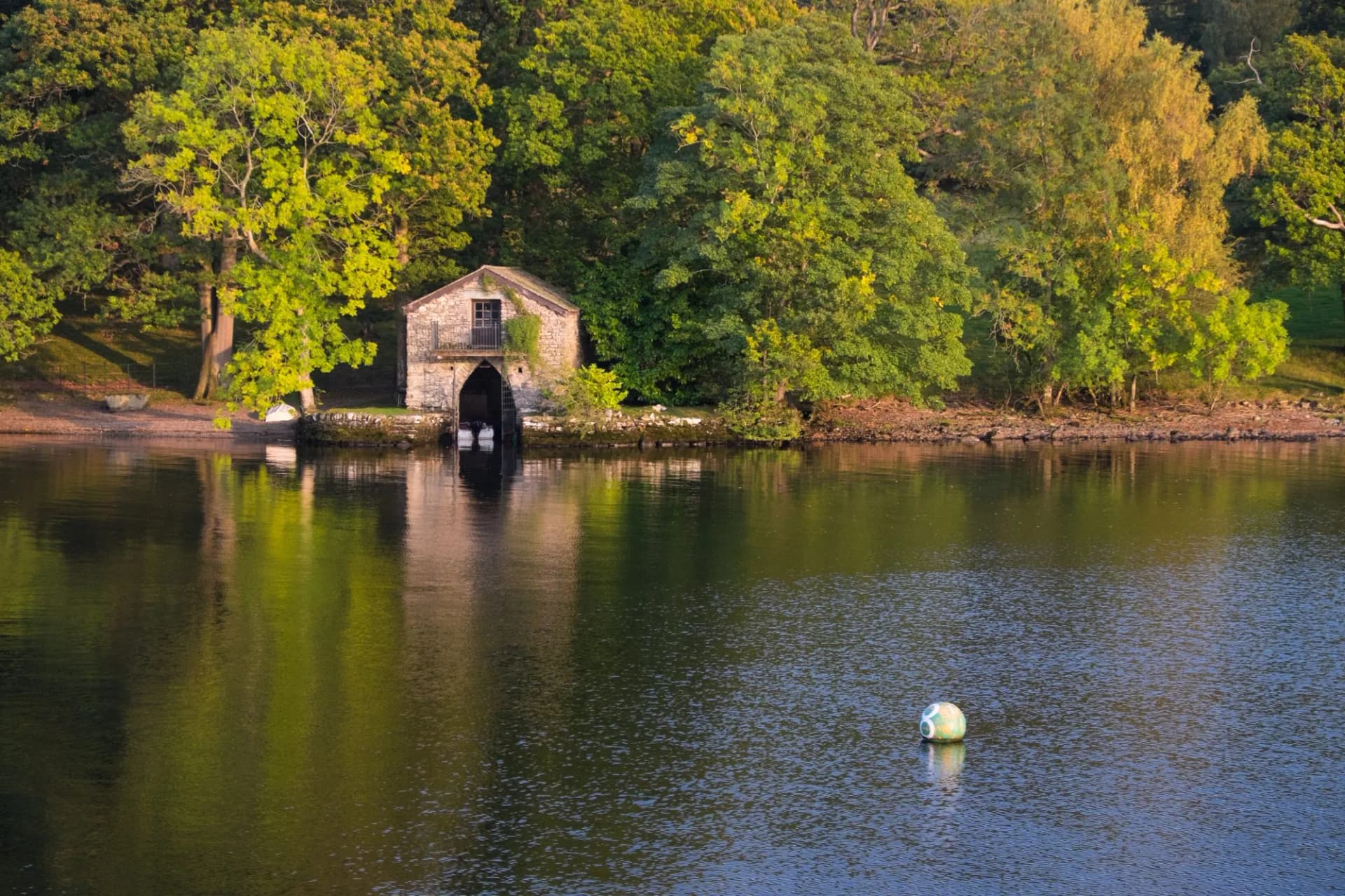 Boat house on Lake Windermere with dense green trees and water reflection.