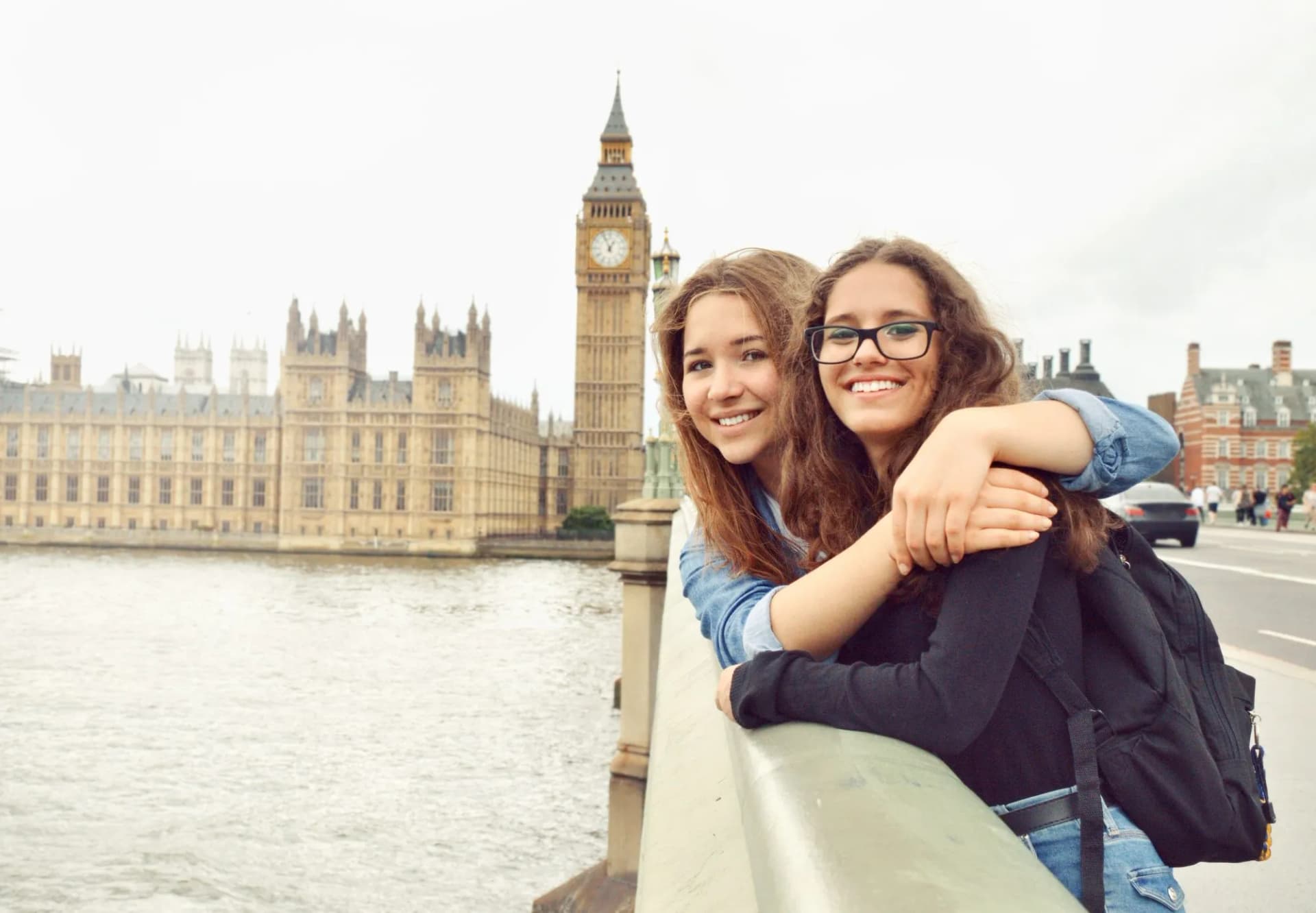 Two smiling girls with backpack by river with Big Ben and Parliament in London