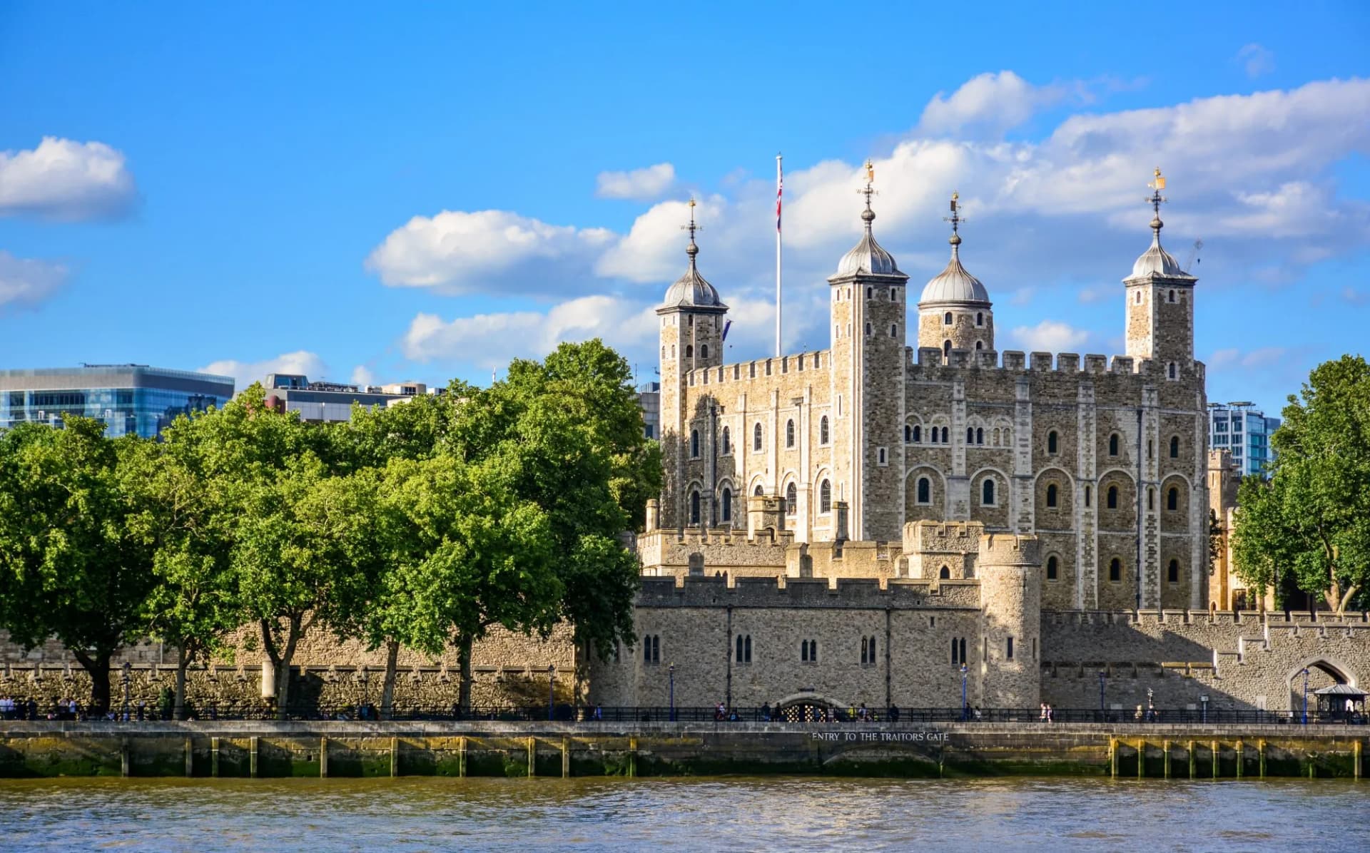 Tower of London castle from the River Thames with green trees and blue sky.