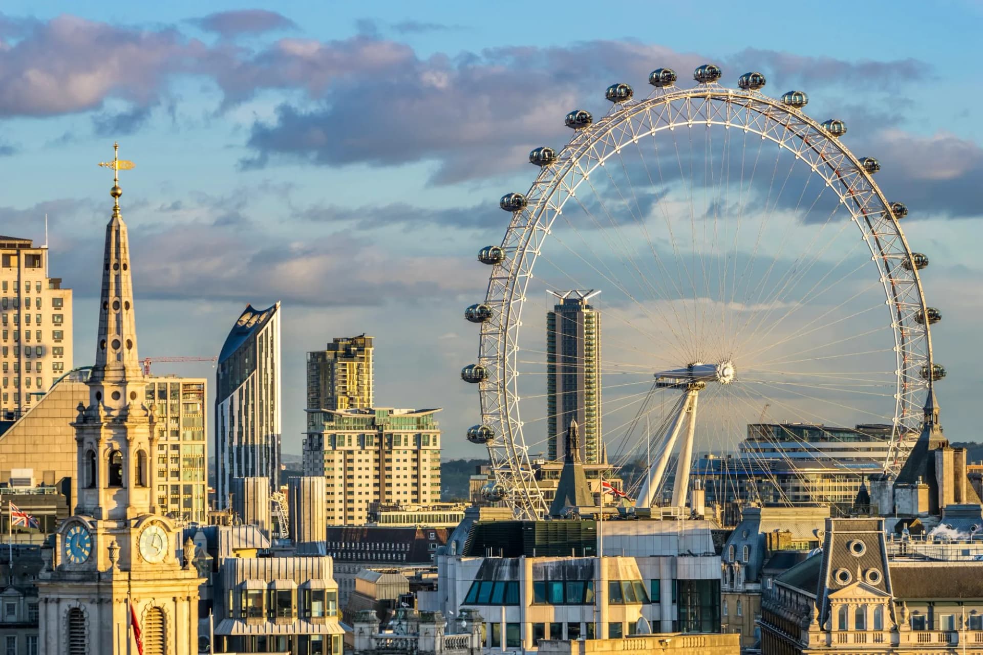 London Eye and historic church spire against modern buildings at sunset.
