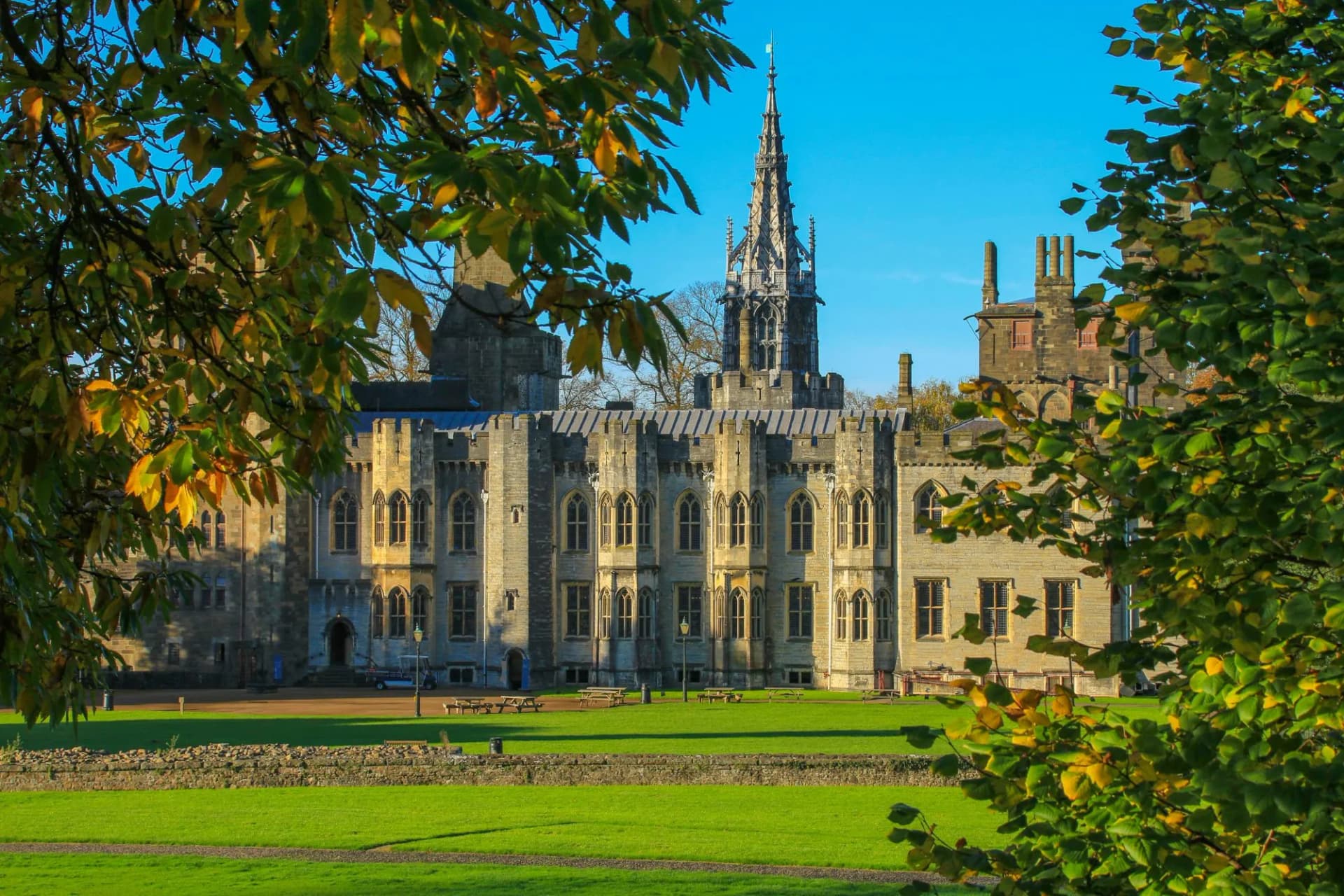 Cardiff Castle exterior with Gothic spire in autumn sunshine, framed by tree leaves.