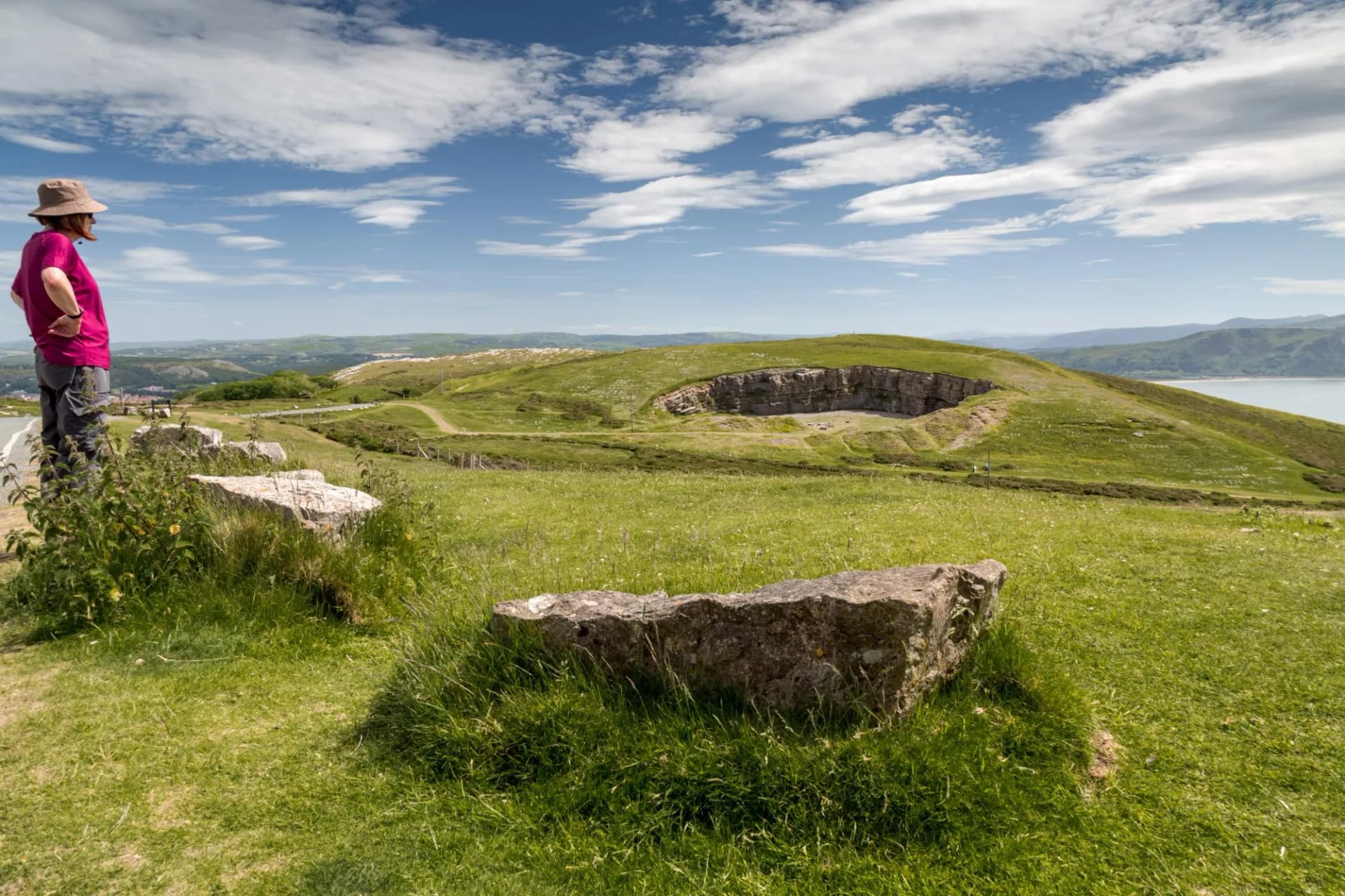Walker on grassy hillside overlooking quarry and Great Orme, Llandudno, Wales.