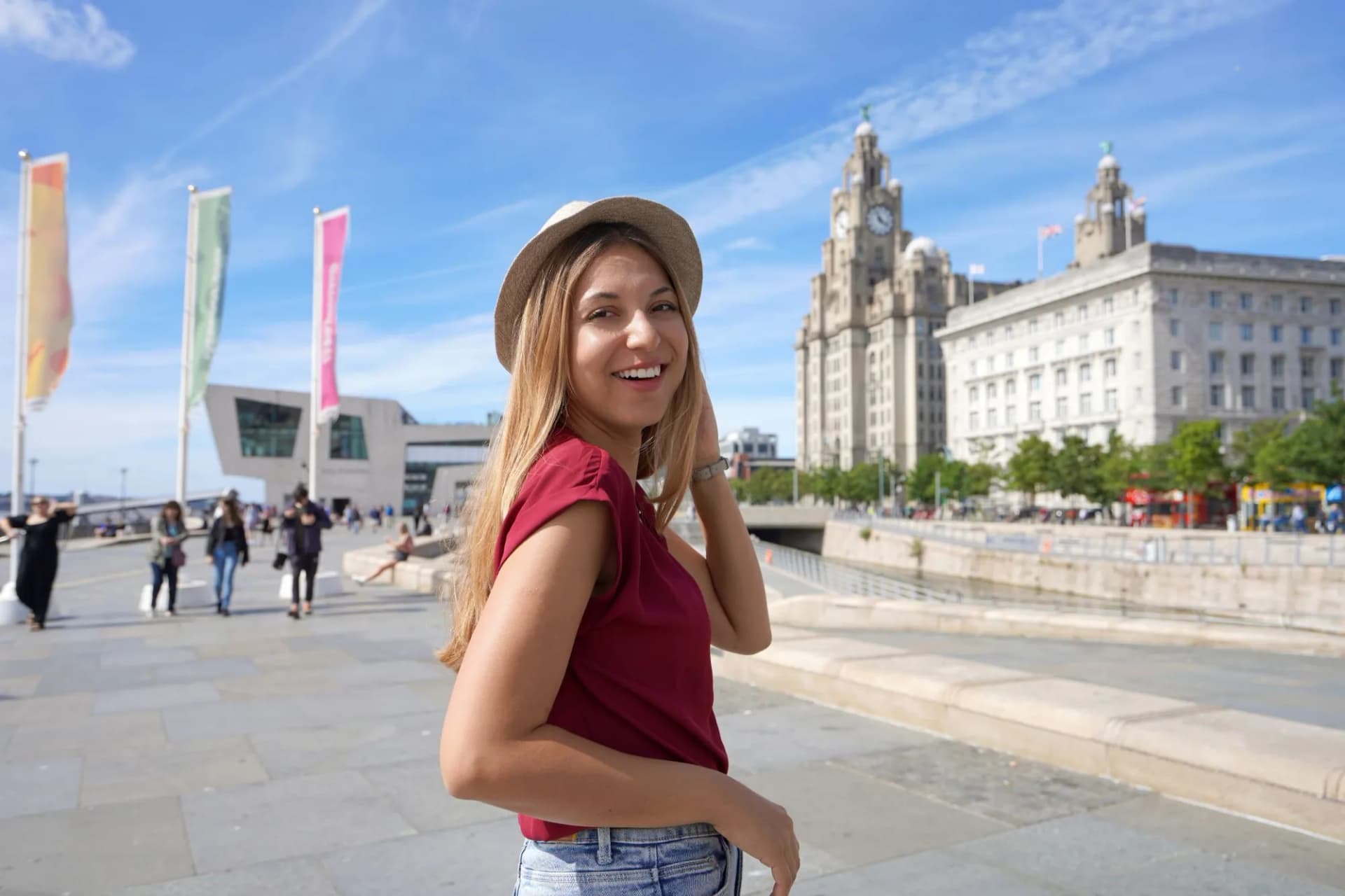 Smiling girl walking on pier head riverside in Liverpool city centre with Liver Building.