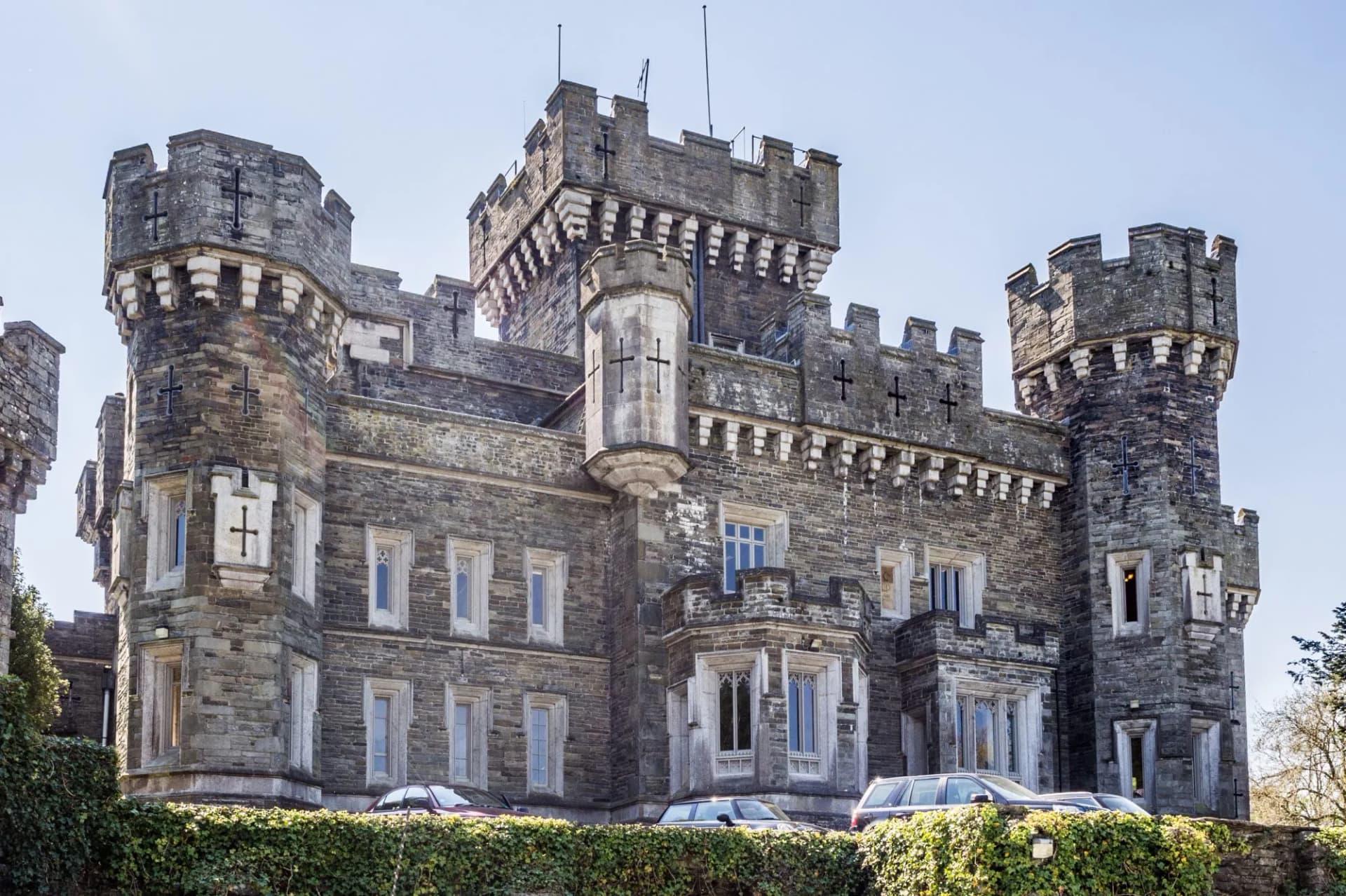 Victorian Neo-Gothic Wray Castle on Lake Windermere shores, Cumbria, UK, with parked cars.