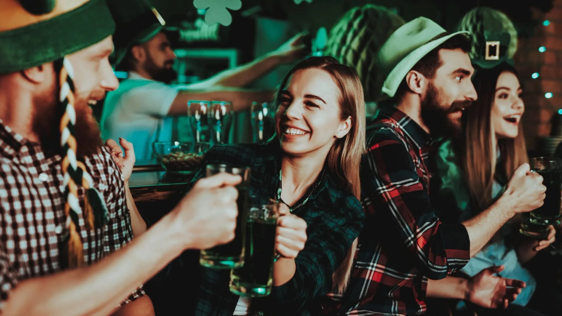 Friends toasting green beer in a dimly lit bar wearing festive hats.