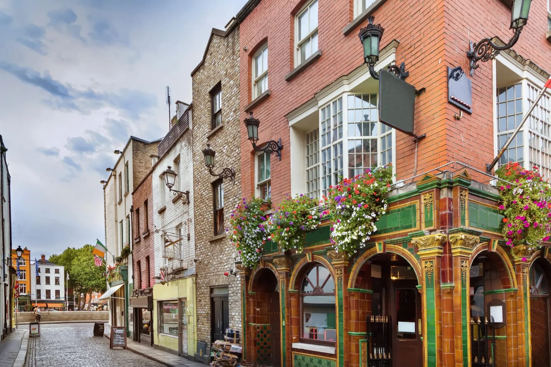 Cobblestone street leading to a pub with ornate tilework and flower boxes in Temple Bar, Dublin, Ireland.