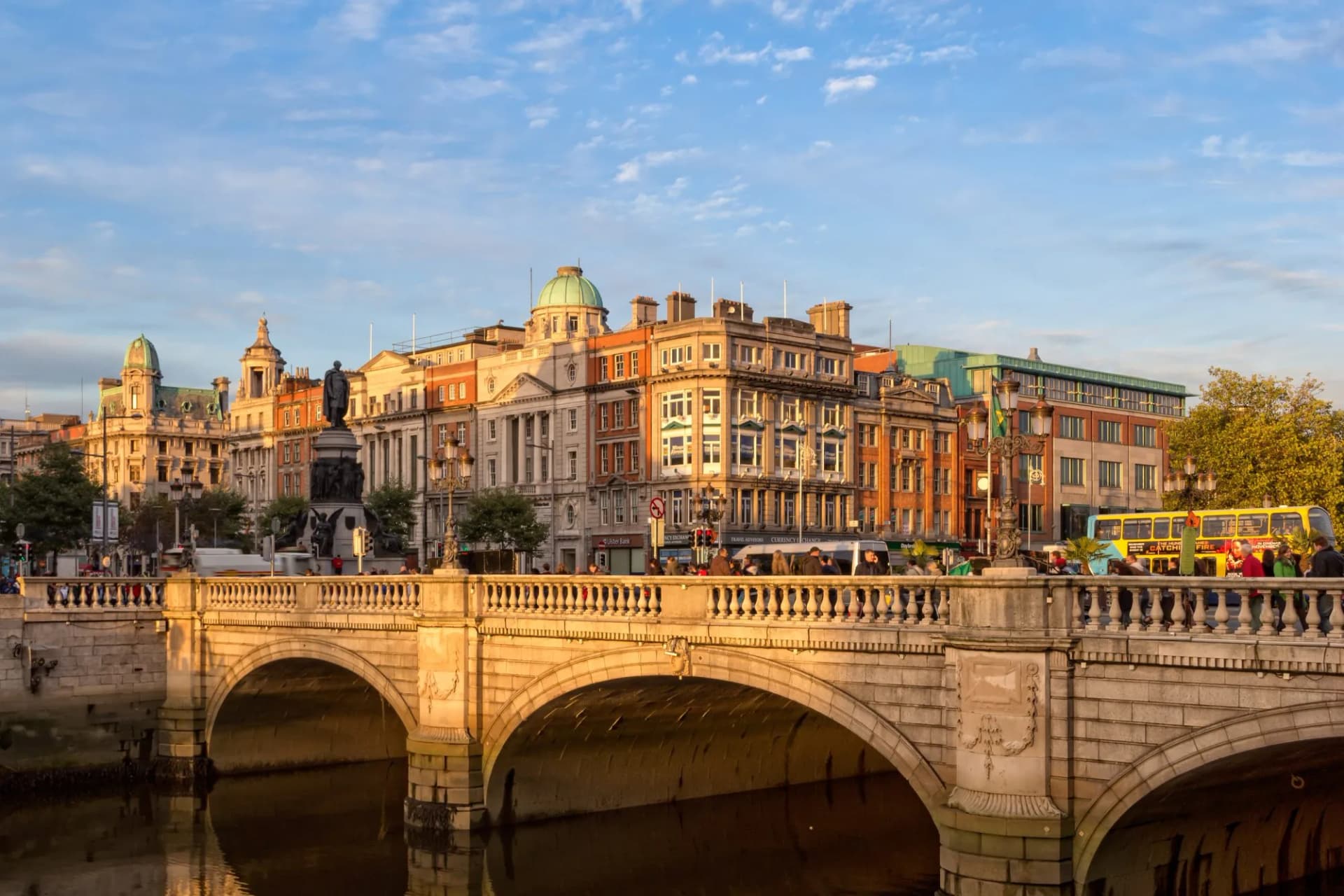 Stone bridge over water with historic buildings and statue in Dublin at sunset