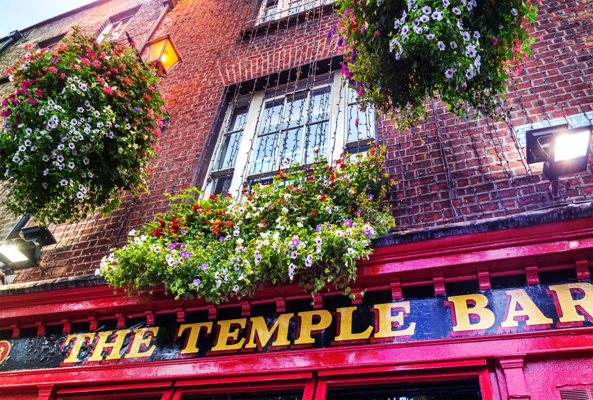 The Temple Bar sign on a red brick building with hanging flower baskets in Dublin, Ireland.