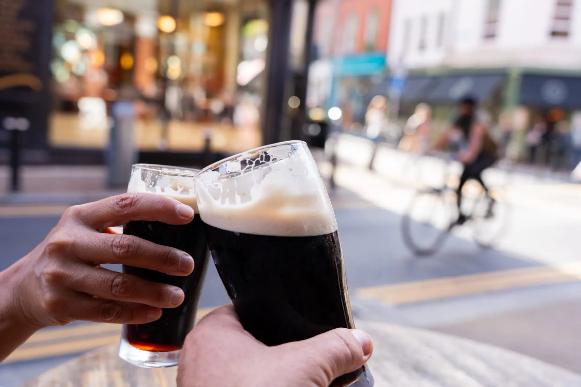 Two hands toasting with Guinness beers on a sunny Central Dublin street in autumn.