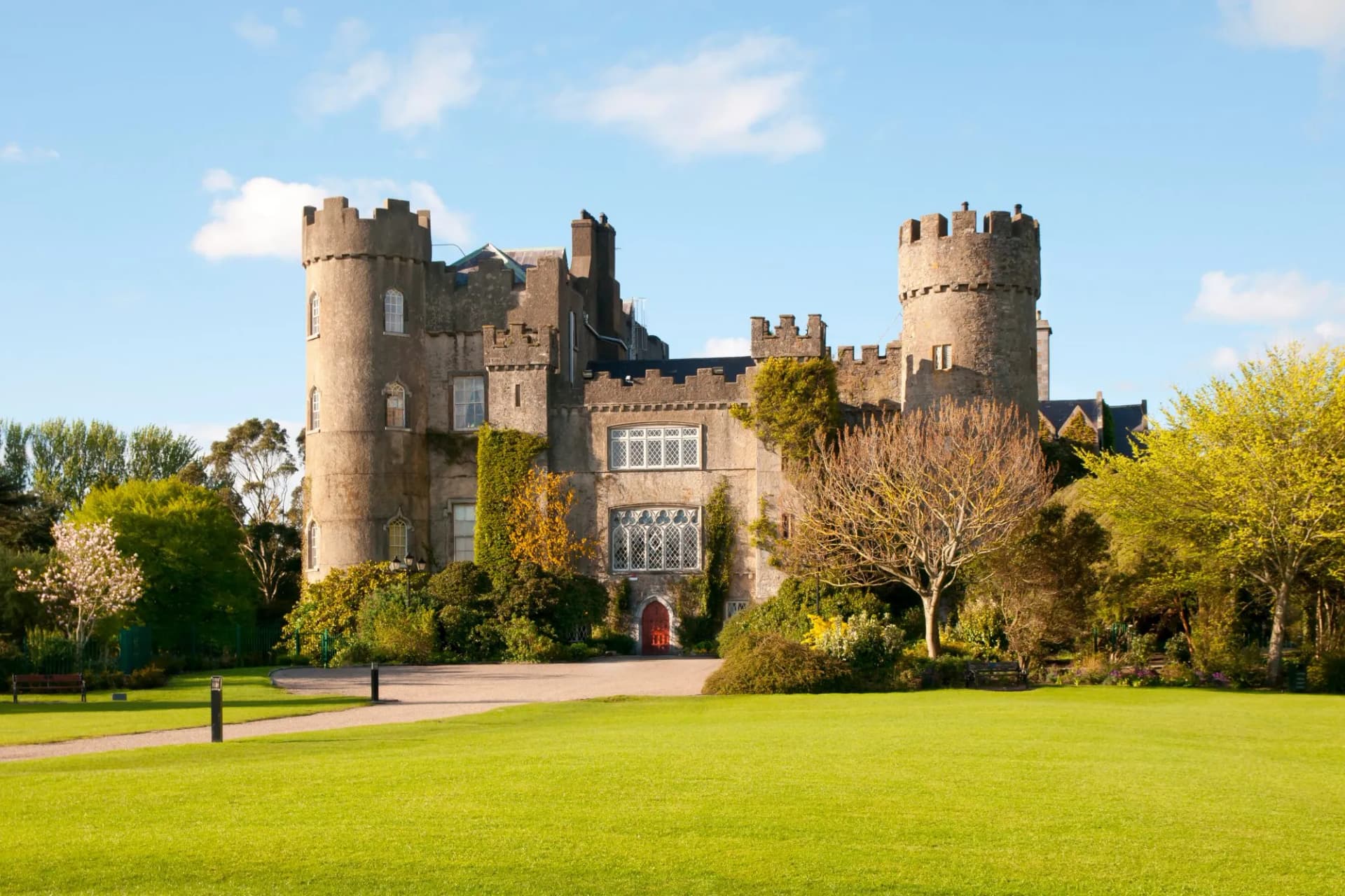 Malahide Castle in Dublin, Ireland, with bright green lawn and trees under a blue sky.
