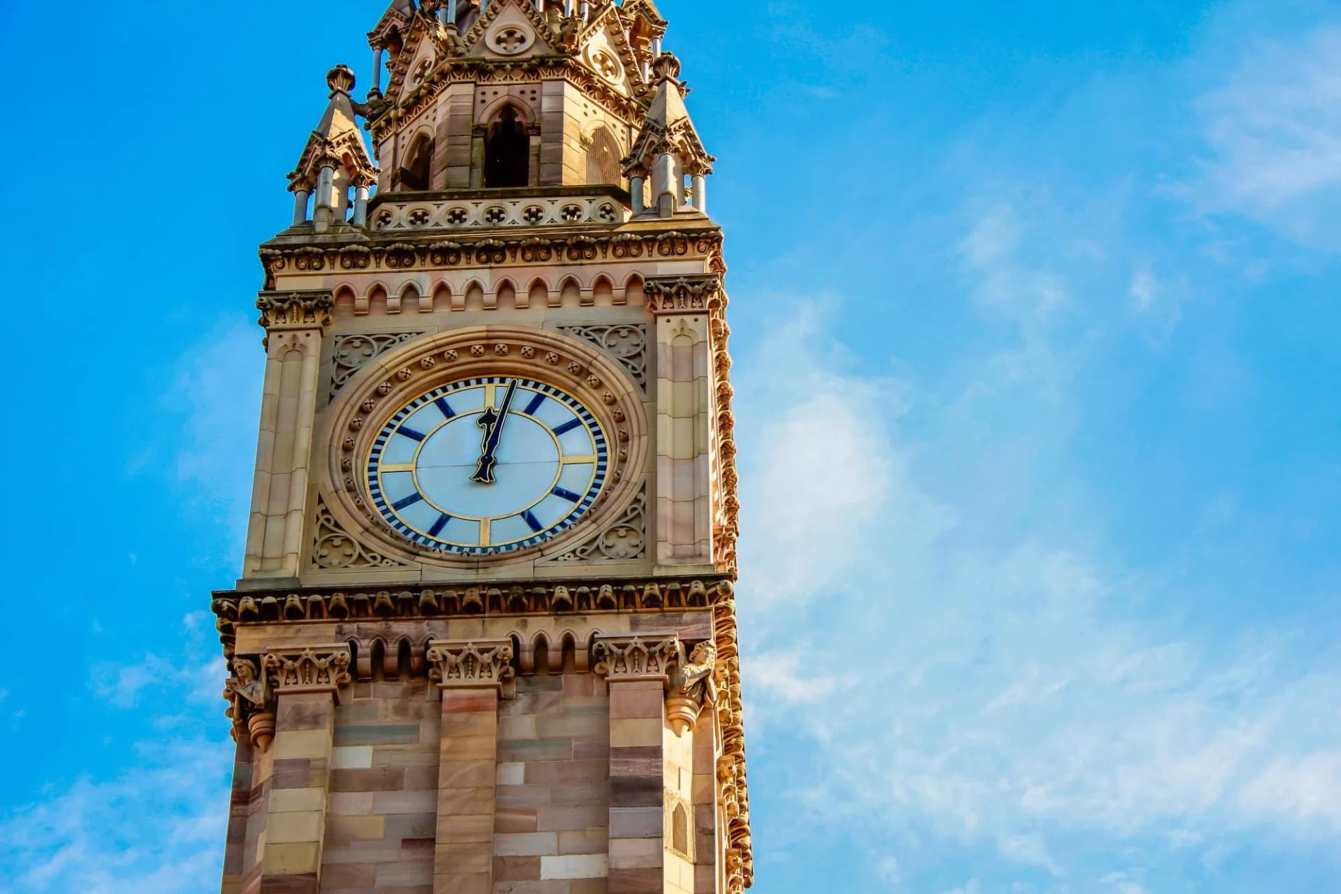 Ornate clock tower detail against a bright blue sky in Belfast, Ireland.
