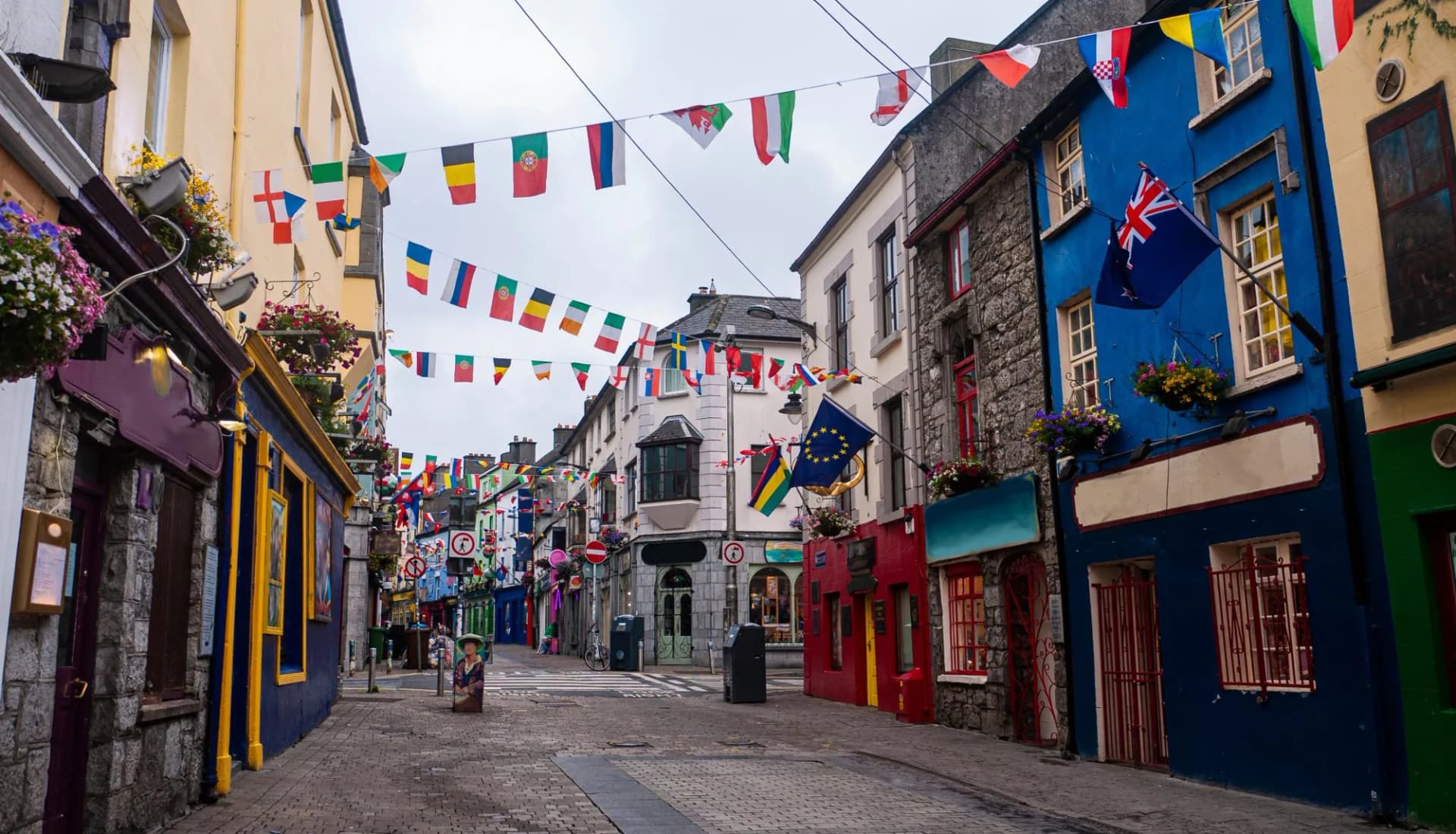 Cobblestone high street in Galway City with brightly painted buildings and international flags strung overhead.