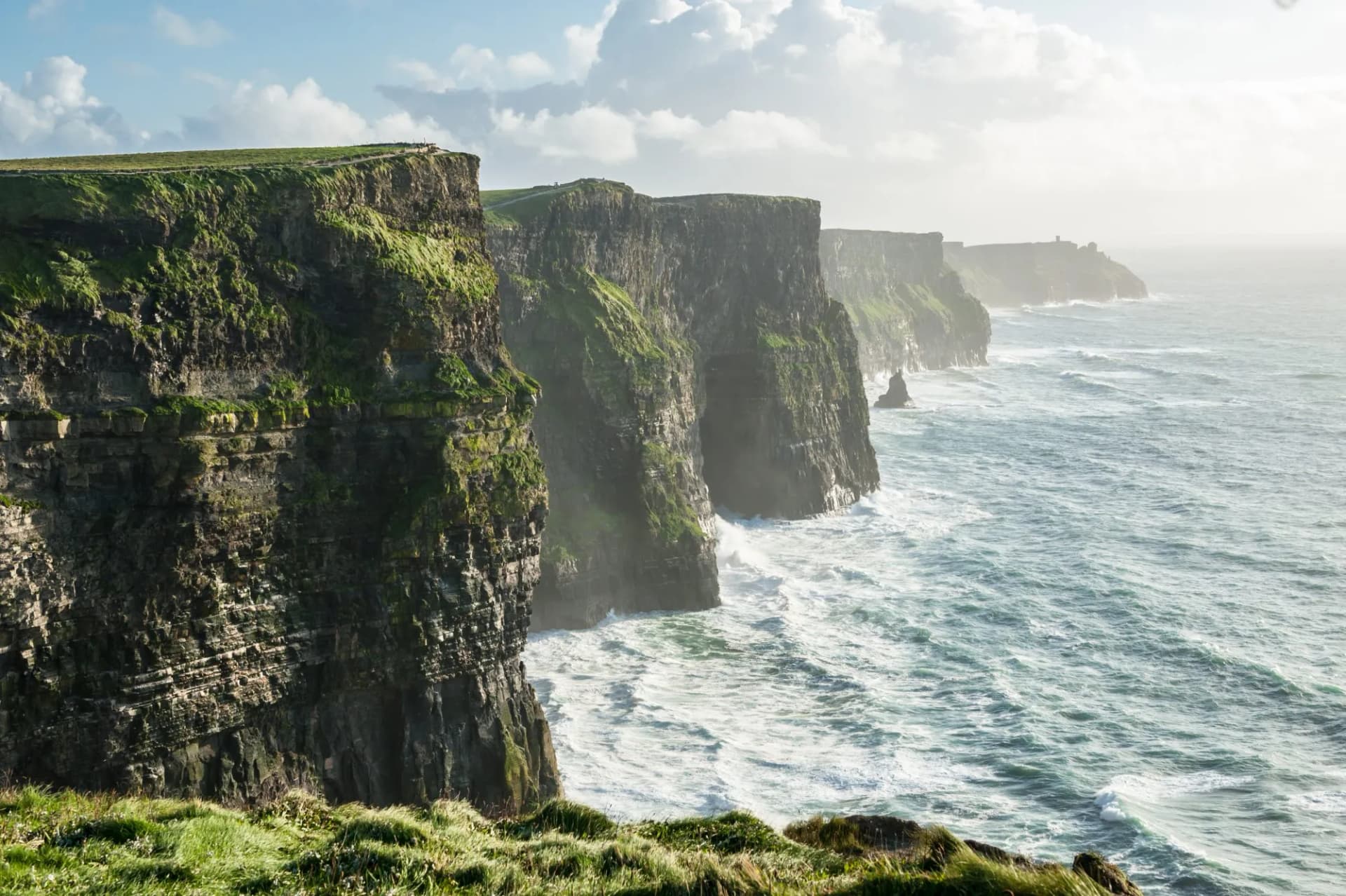 Cliffs of Moher, Ireland, featuring steep green cliffs meeting rough, white-capped Atlantic Ocean waves.