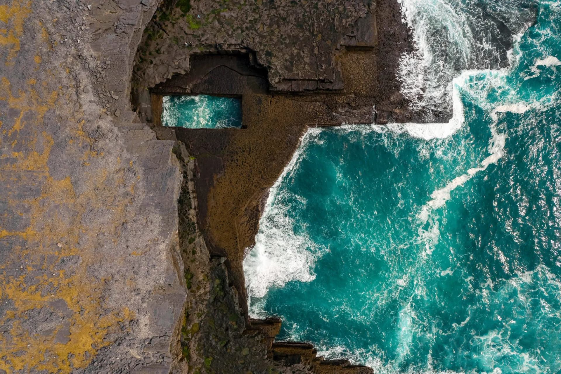 Aerial view of Poll na bPeist wormhole, Inishmore, Aran Island, Ireland, with turquoise ocean water.