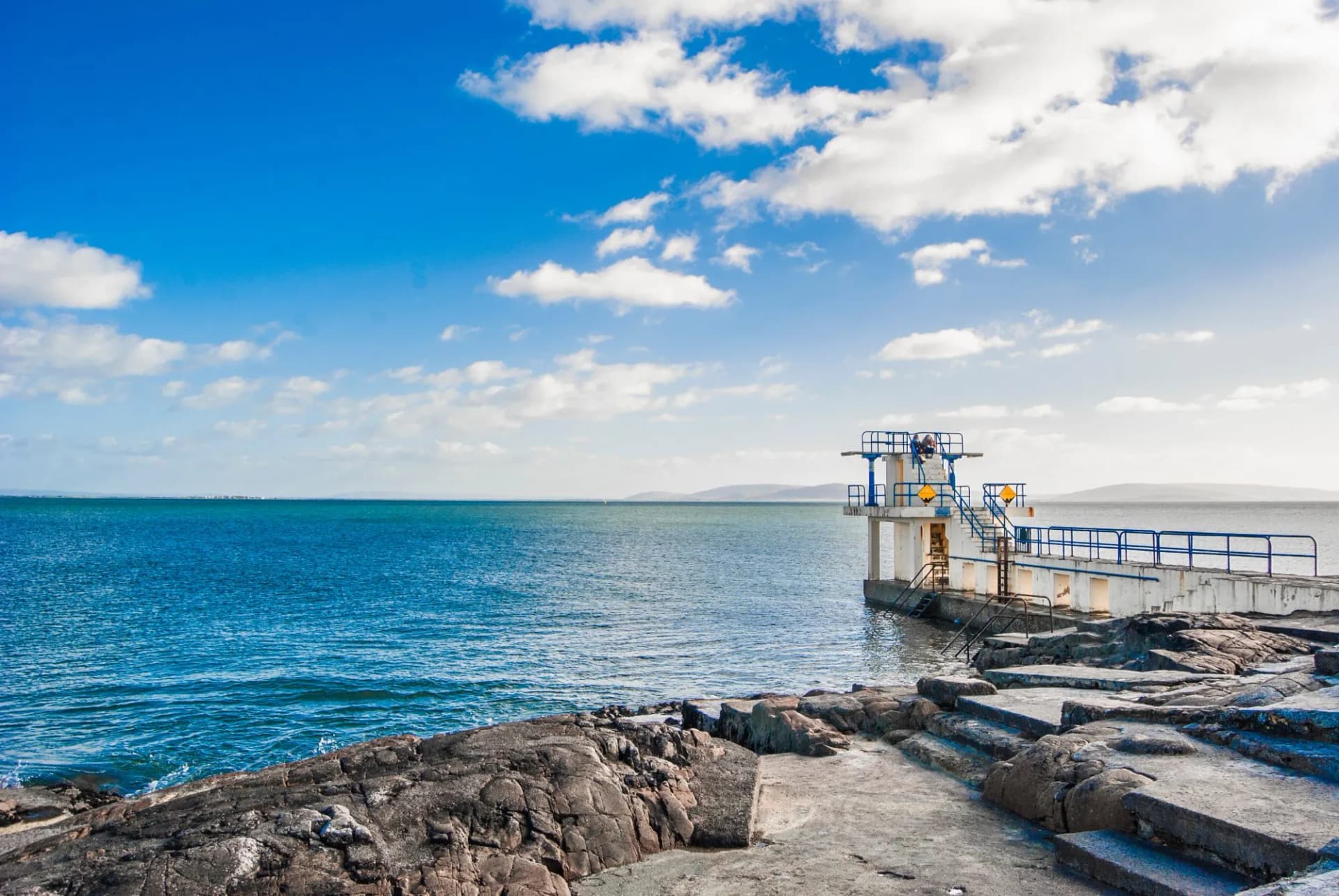 Salthill diving board overlooking Galway Bay, Ireland, with blue sky and rocky shore.